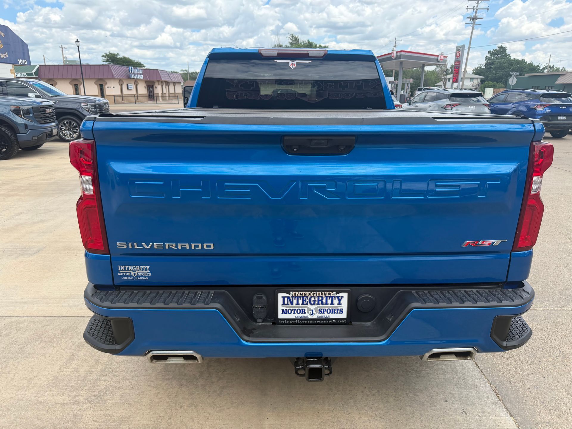 Blue Chevrolet Silverado rear view in a parking lot, with chrome bumper and hitch.