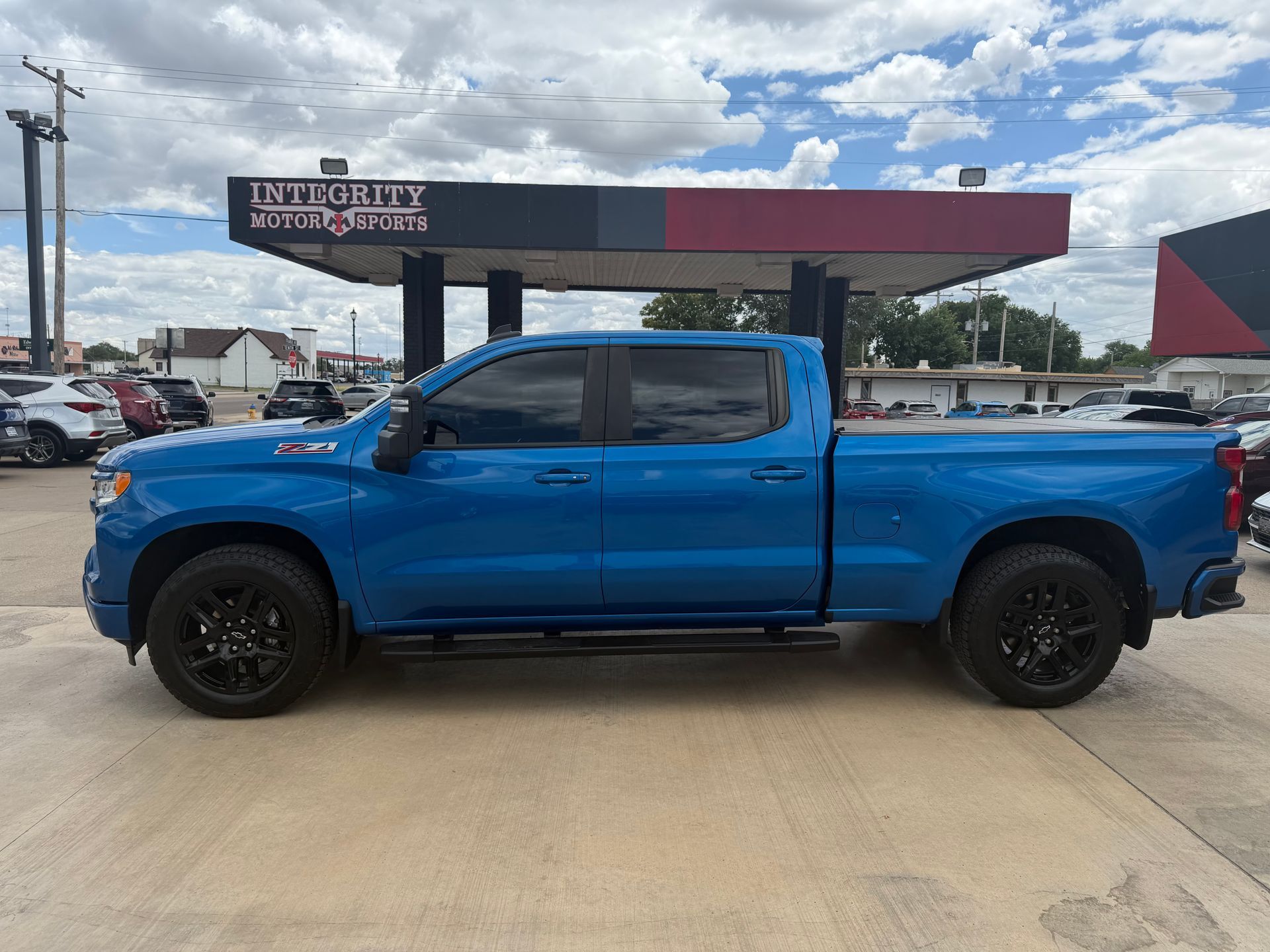 Blue pickup truck parked at a dealership under a cloudy sky