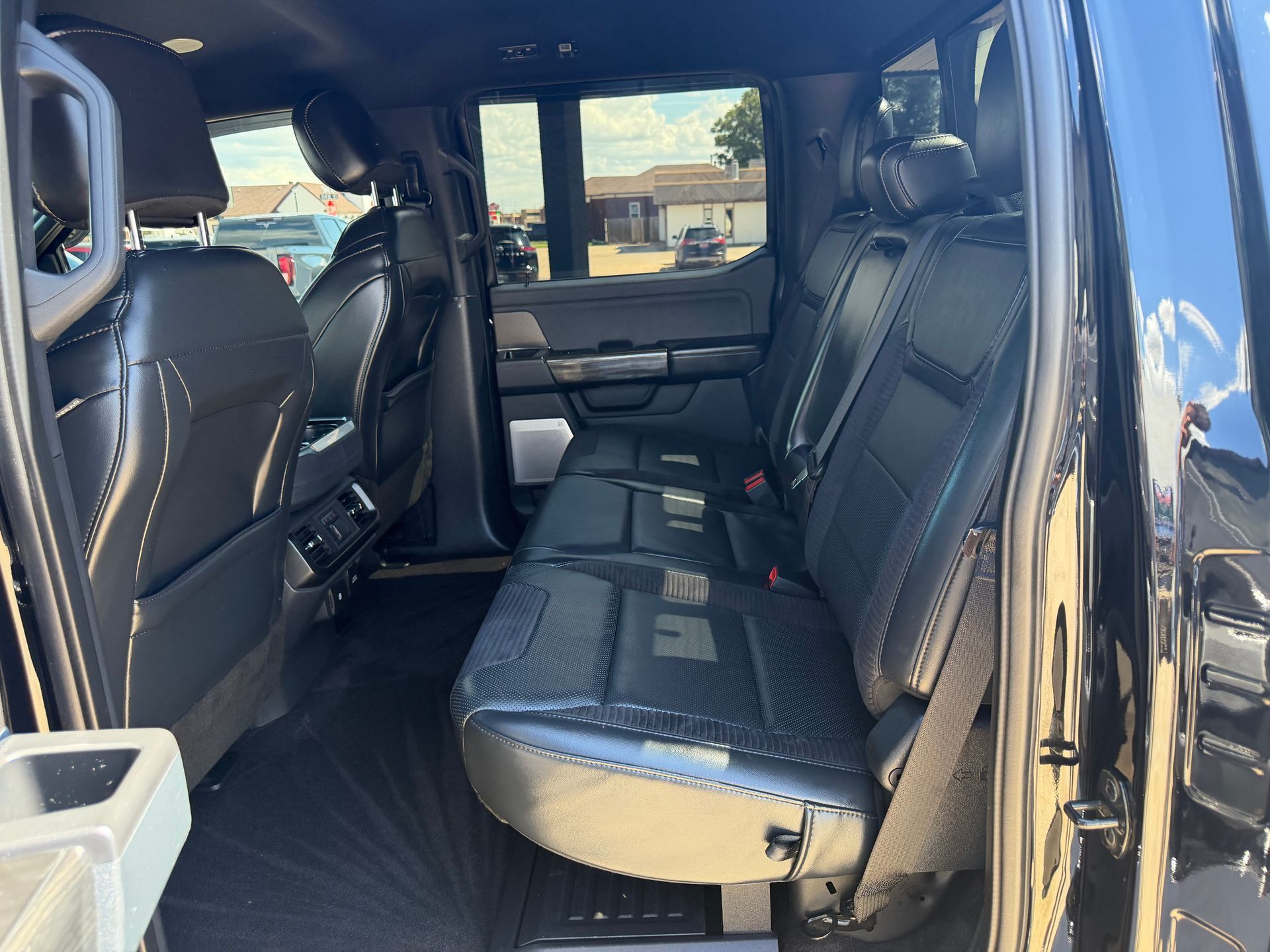 Black leather truck back seat with center armrest and open door, viewed from the side