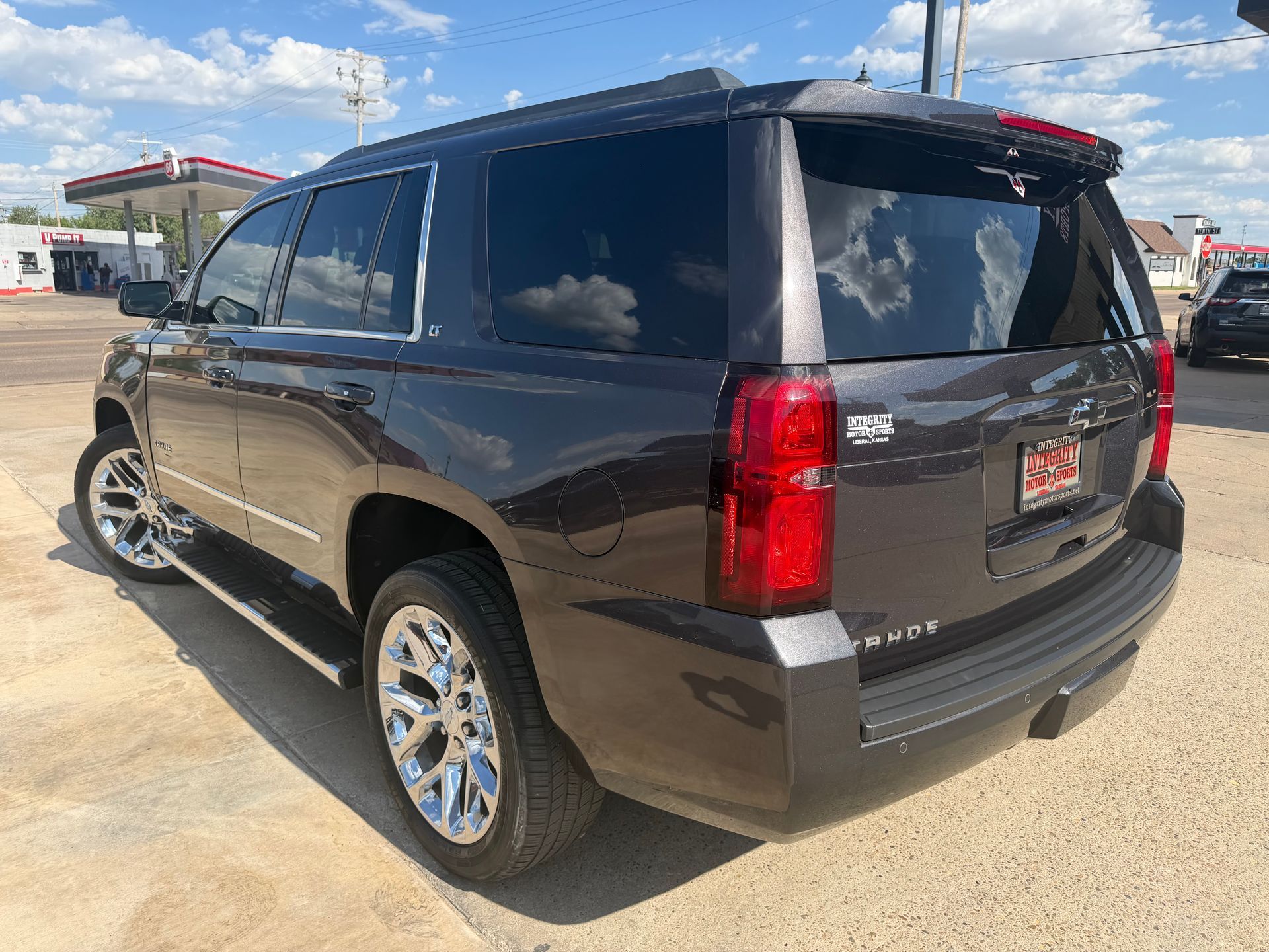 Black SUV parked on a sandy lot near a gas station, viewed from the rear side.