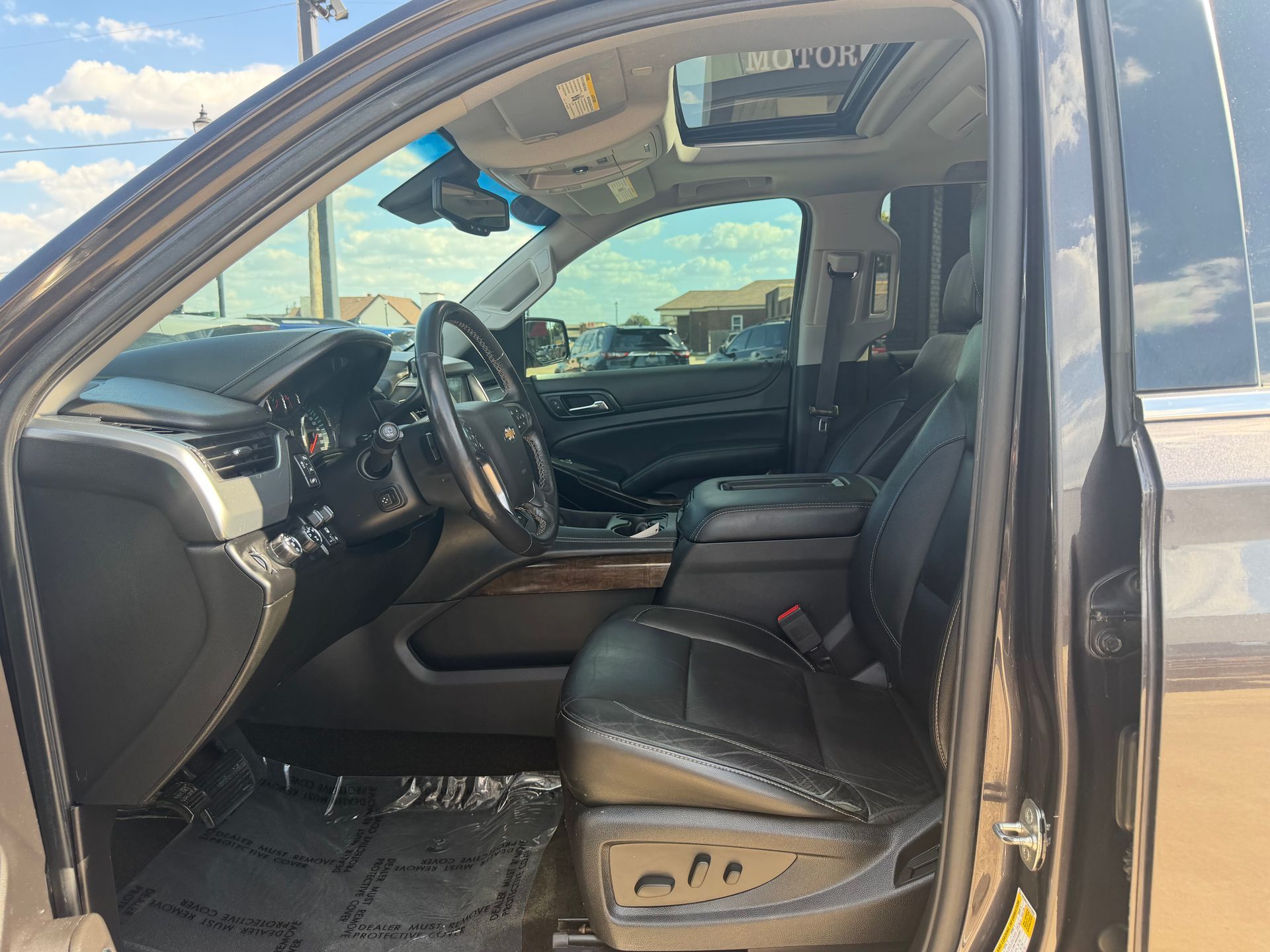 Open car door showing black leather driver’s seat and dashboard interior under bright daylight.