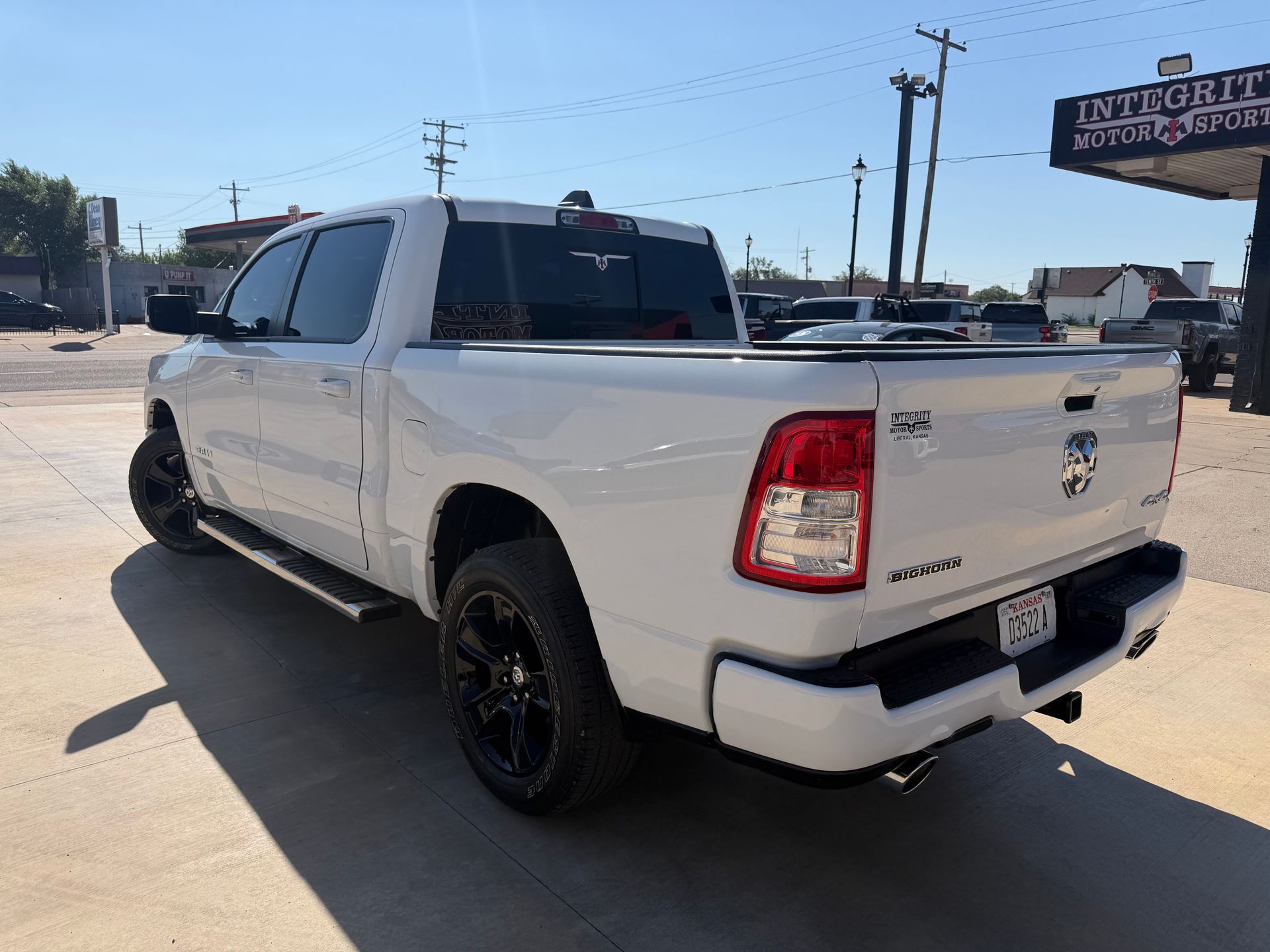 White pickup truck with black wheels parked in a sunny lot, rear three-quarter view