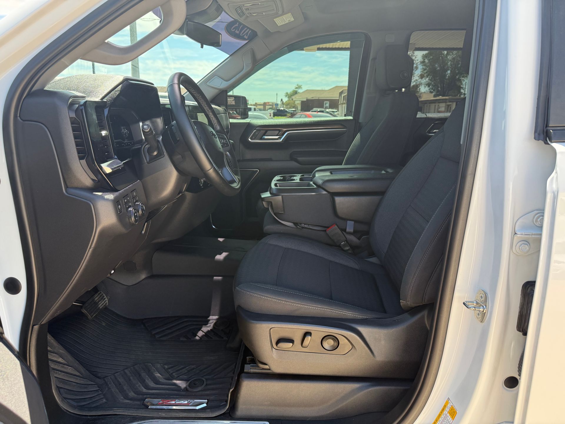 Interior of a white truck with black seats and floor mats. Sunlight streams through the window.