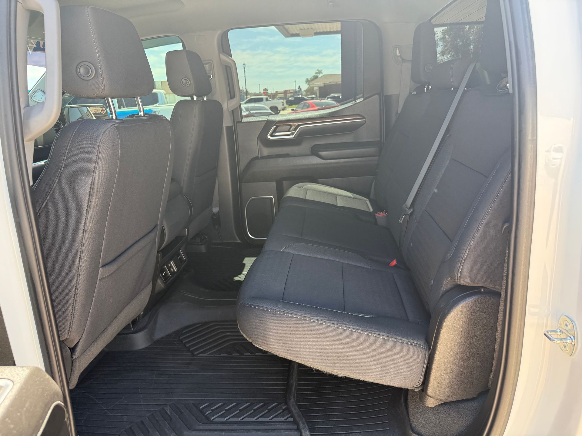 Interior of a pickup truck's back seat; black seats, rubber floor mats, and window.