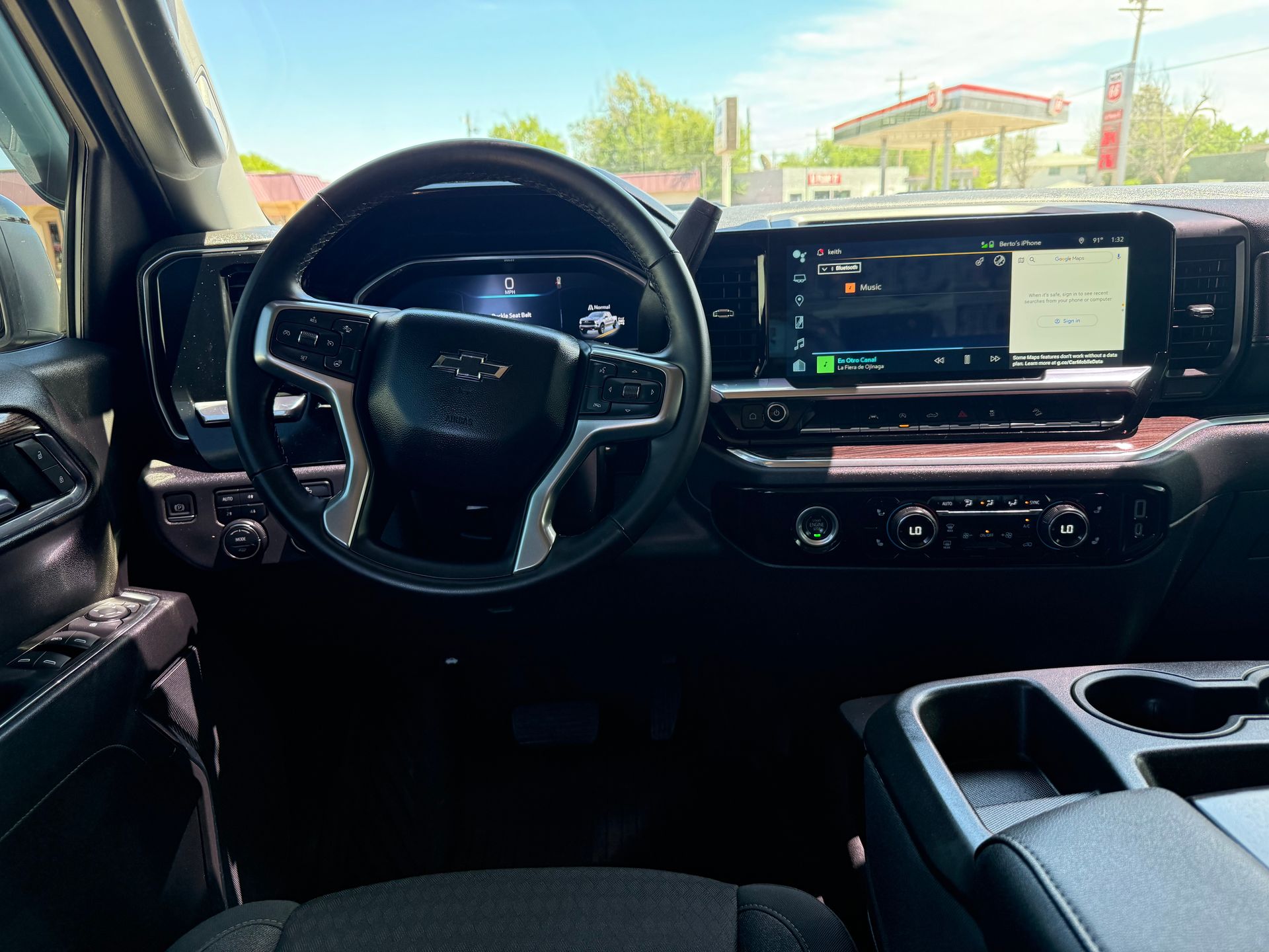 Interior of a black Chevrolet truck. Steering wheel, large touchscreen, dashboard controls, and cup holders are visible.