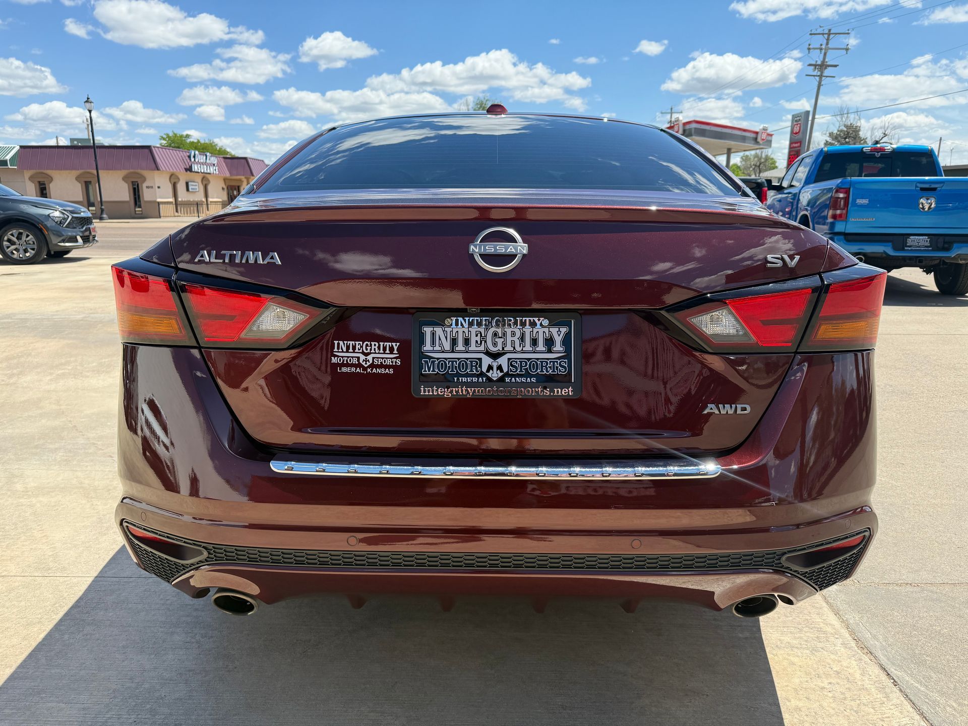 Dark red Nissan Altima sedan with license plate; parked outdoors on a sunny day.