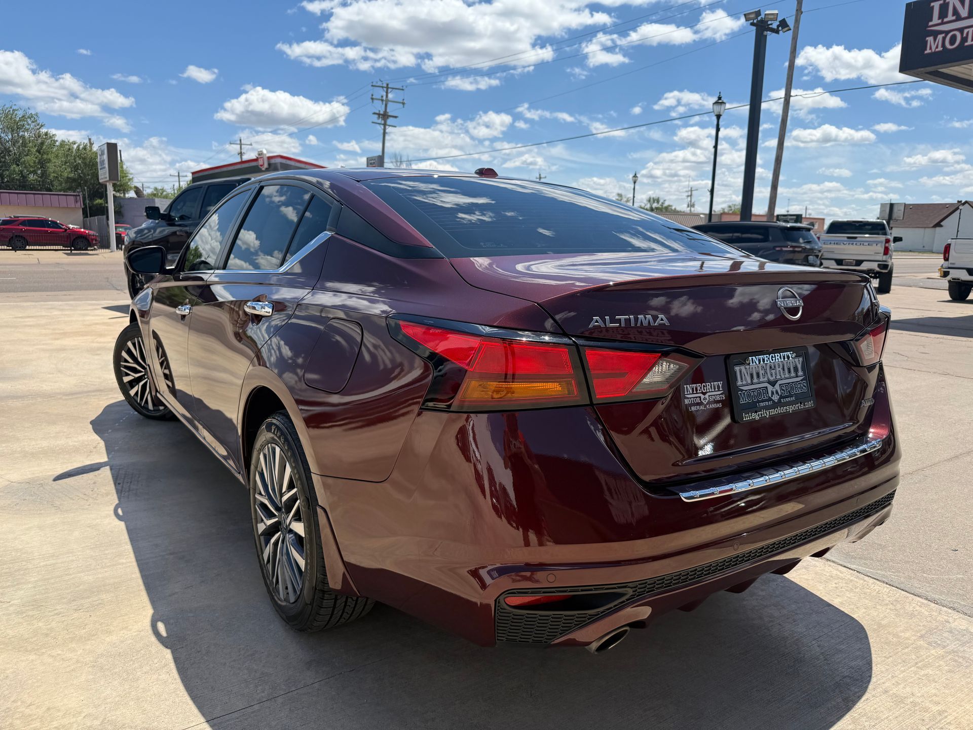 Dark red Nissan Altima sedan parked on a concrete lot under a blue sky.