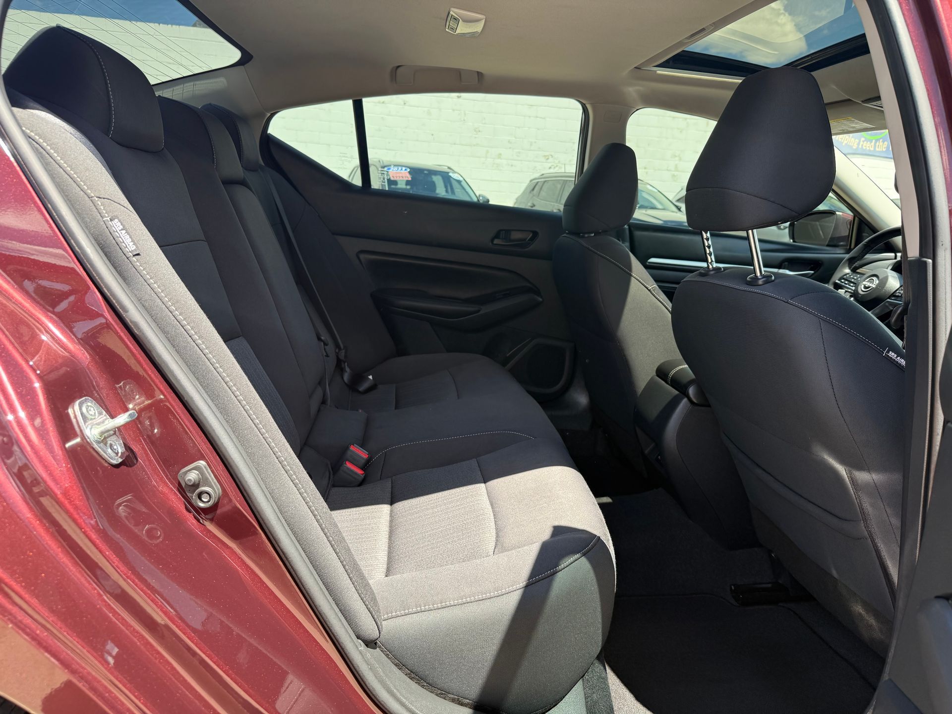 Interior of a red car, showing rear seats, dark grey fabric, and headrests. Sunlight visible through windows.