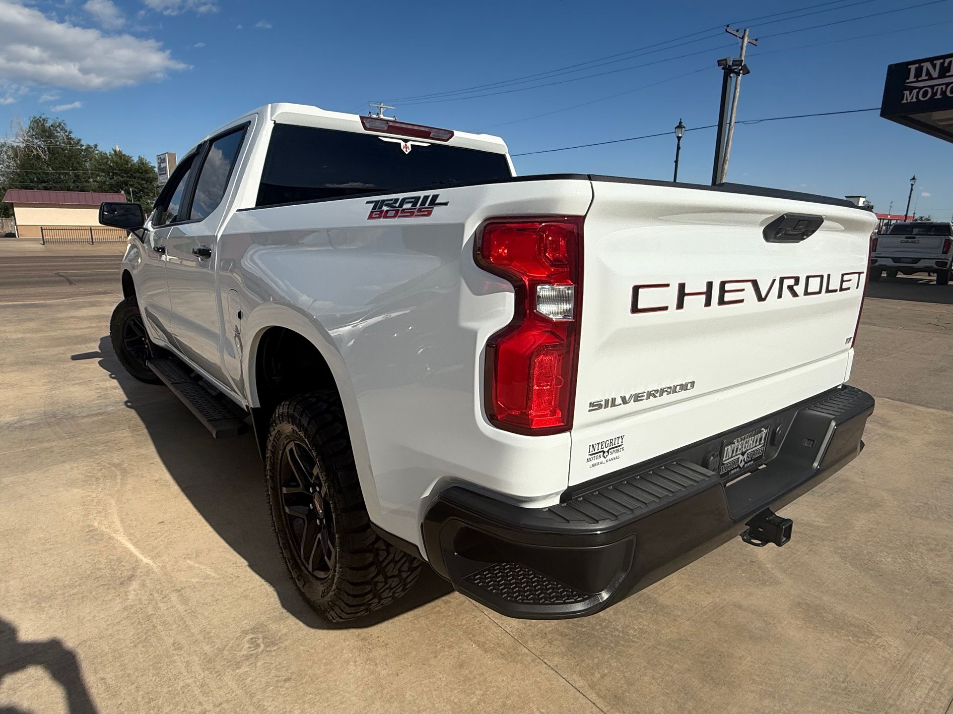 White Chevrolet Silverado pickup truck, rear view, parked outdoors. Black tires and trim; CHEVROLET on tailgate.