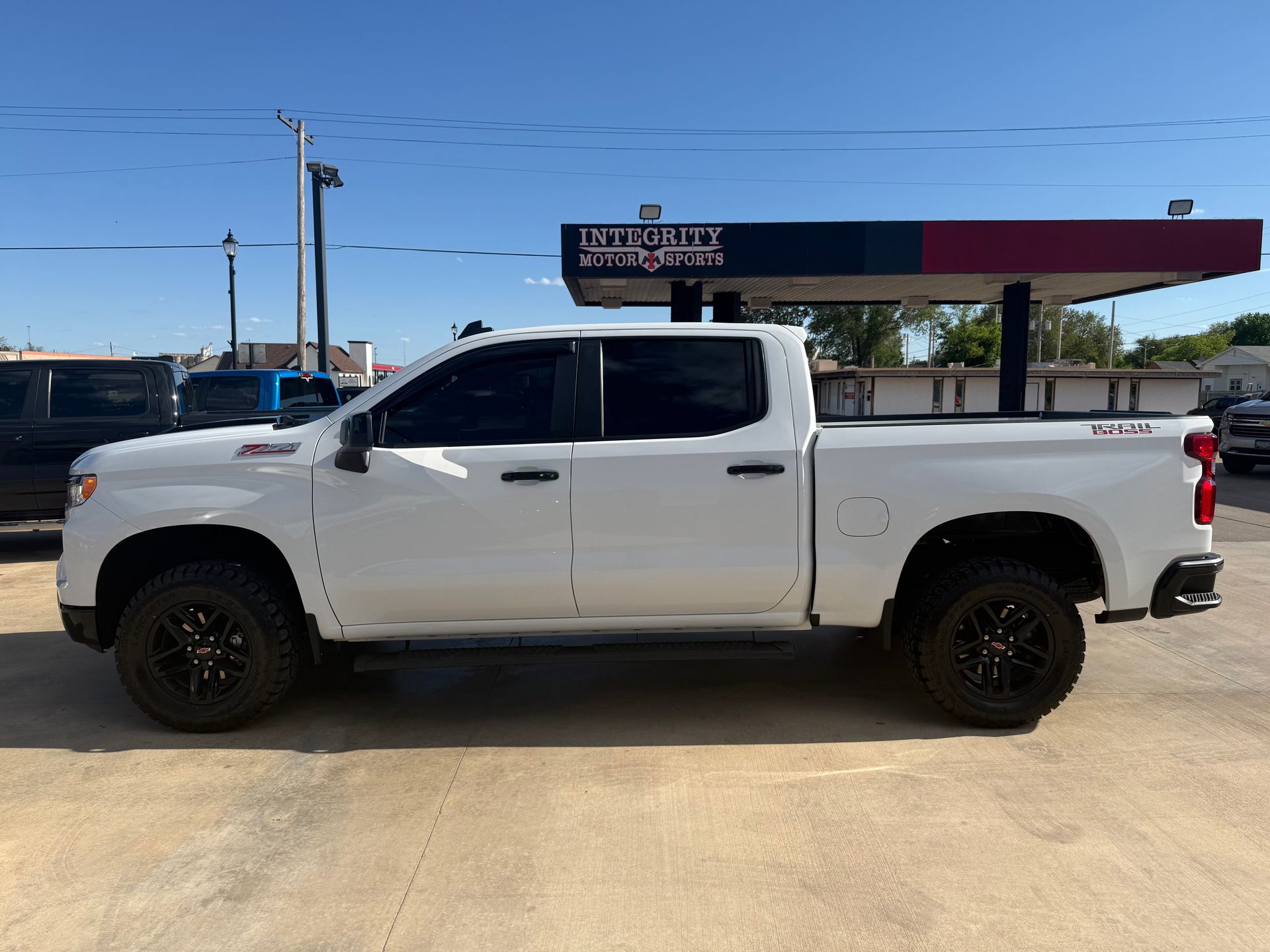 White Chevrolet truck with black wheels parked outside a business under a blue sky.