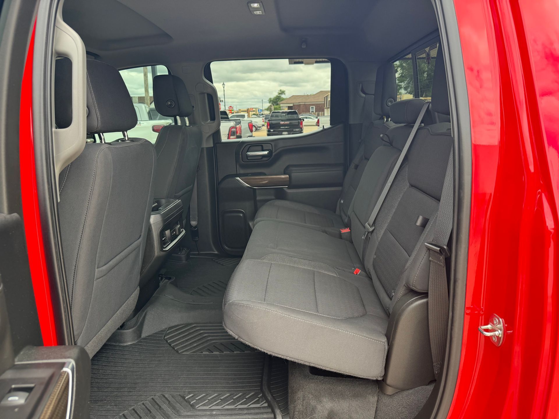Interior view of a red pickup truck's back seat. Black seats, door open.