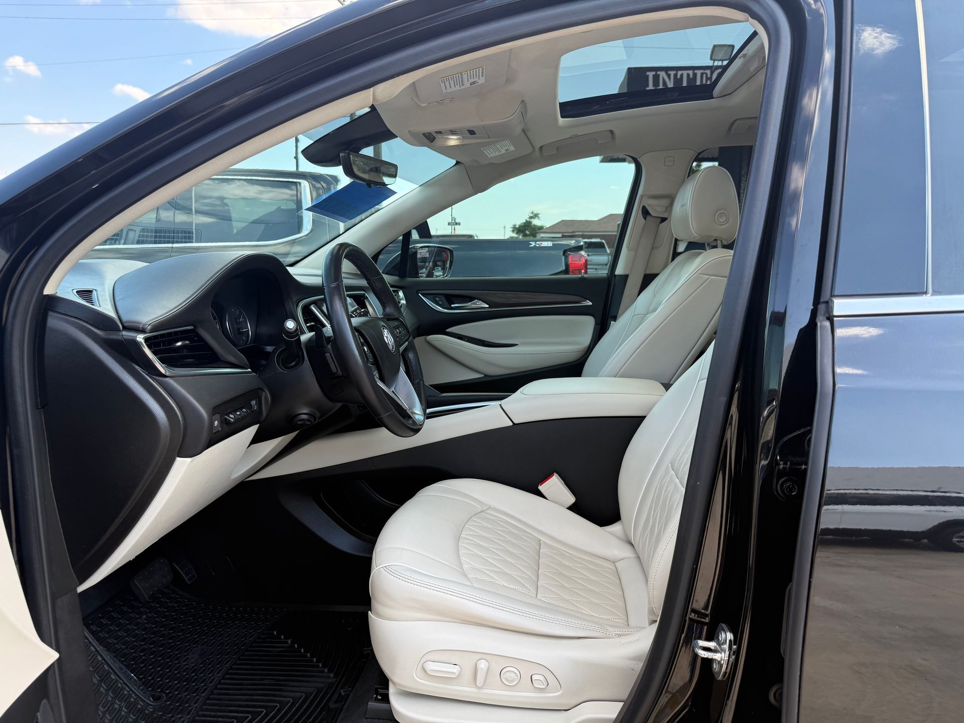 Black car interior with white leather seats, steering wheel, and open sunroof.