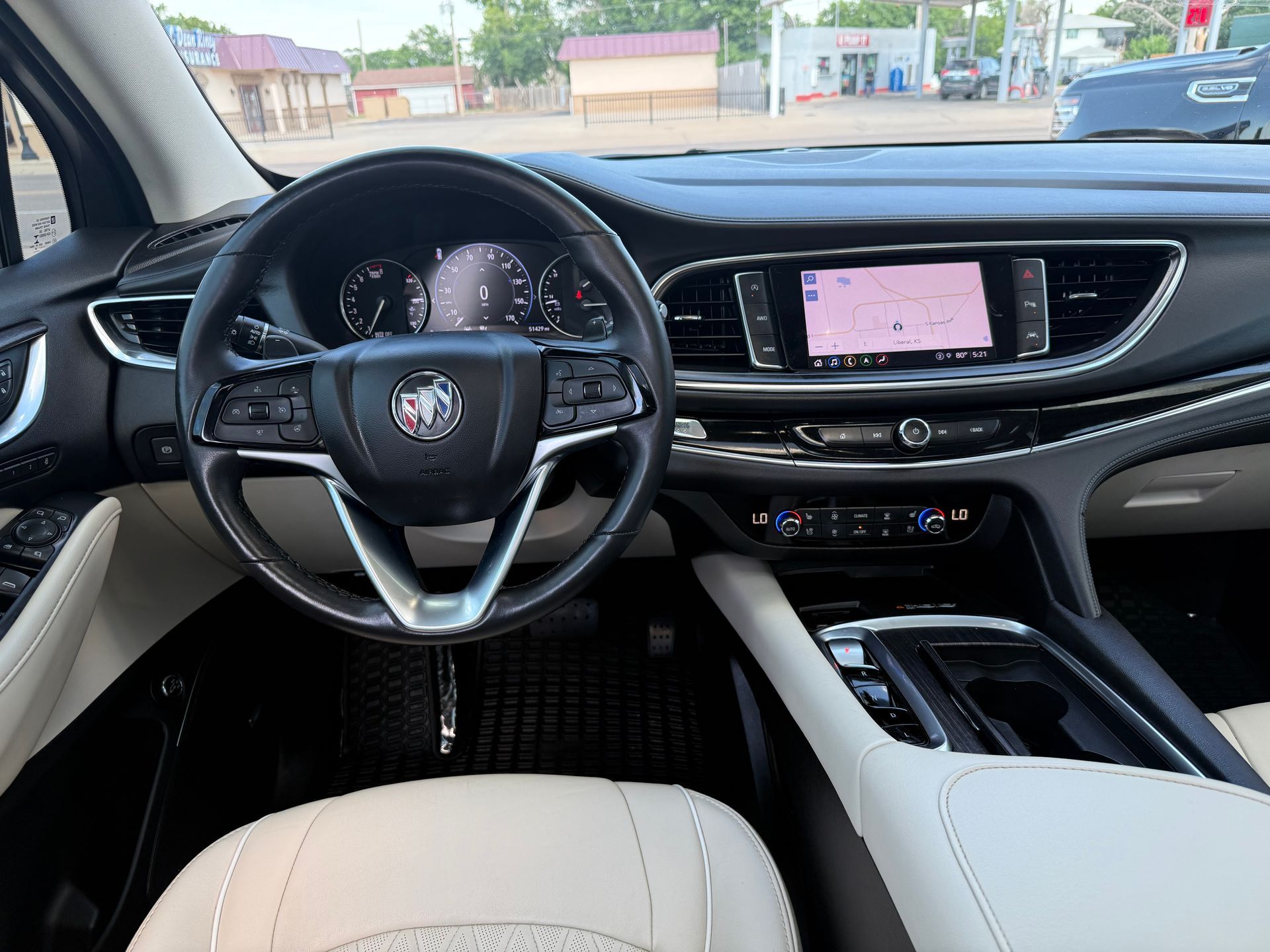 Interior of a Buick SUV. Black dashboard with a steering wheel, infotainment screen, and cream-colored seats.