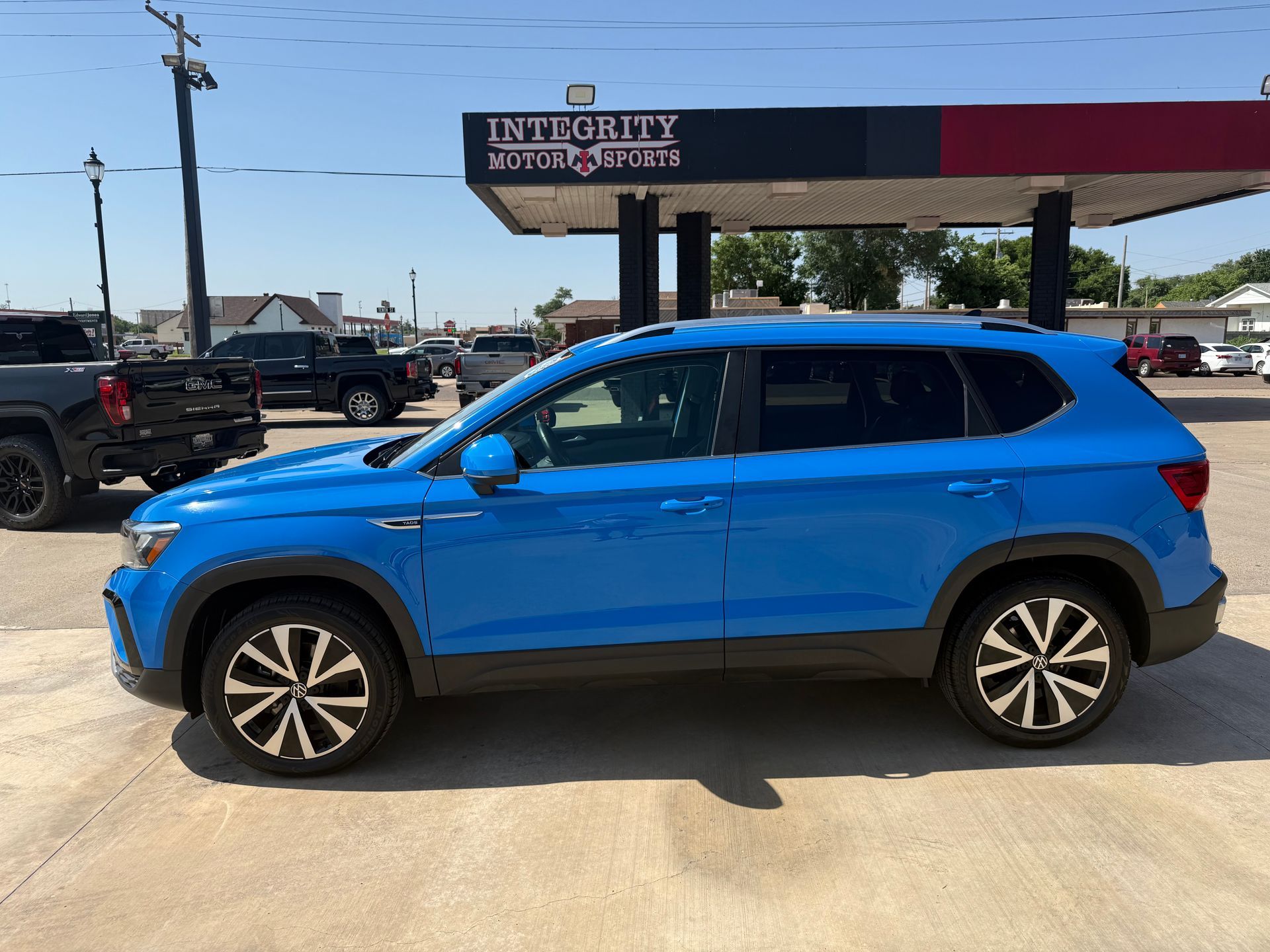 Blue Volkswagen Taos SUV parked in front of a car dealership on a sunny day.
