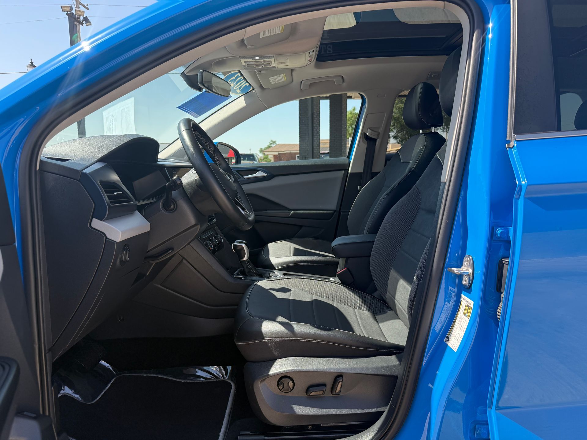 Blue car interior with black seats and dashboard. Open door shows driver's side.