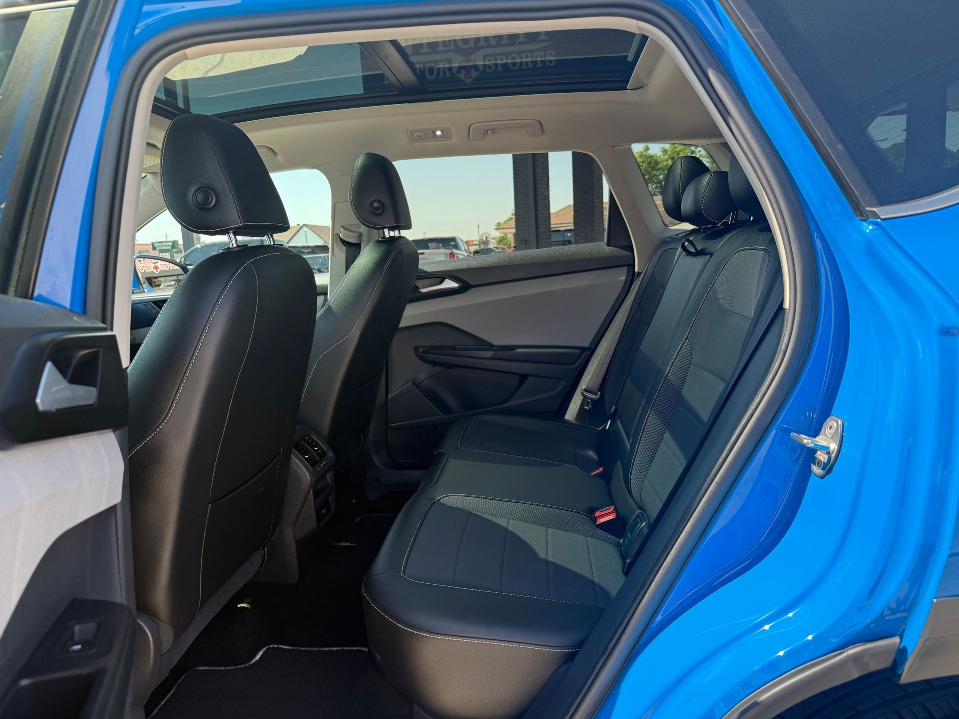 Rear interior of a blue car, black seats, sunroof, sunlight.
