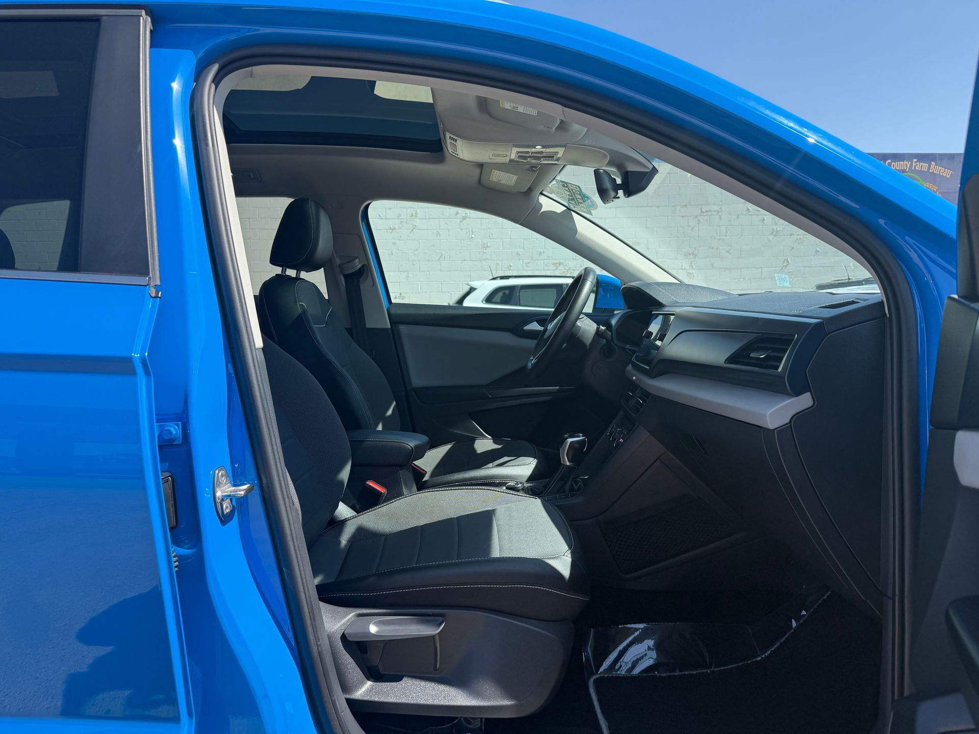 Blue car interior, driver's seat visible. Black and gray seats, dashboard, and steering wheel in daylight.