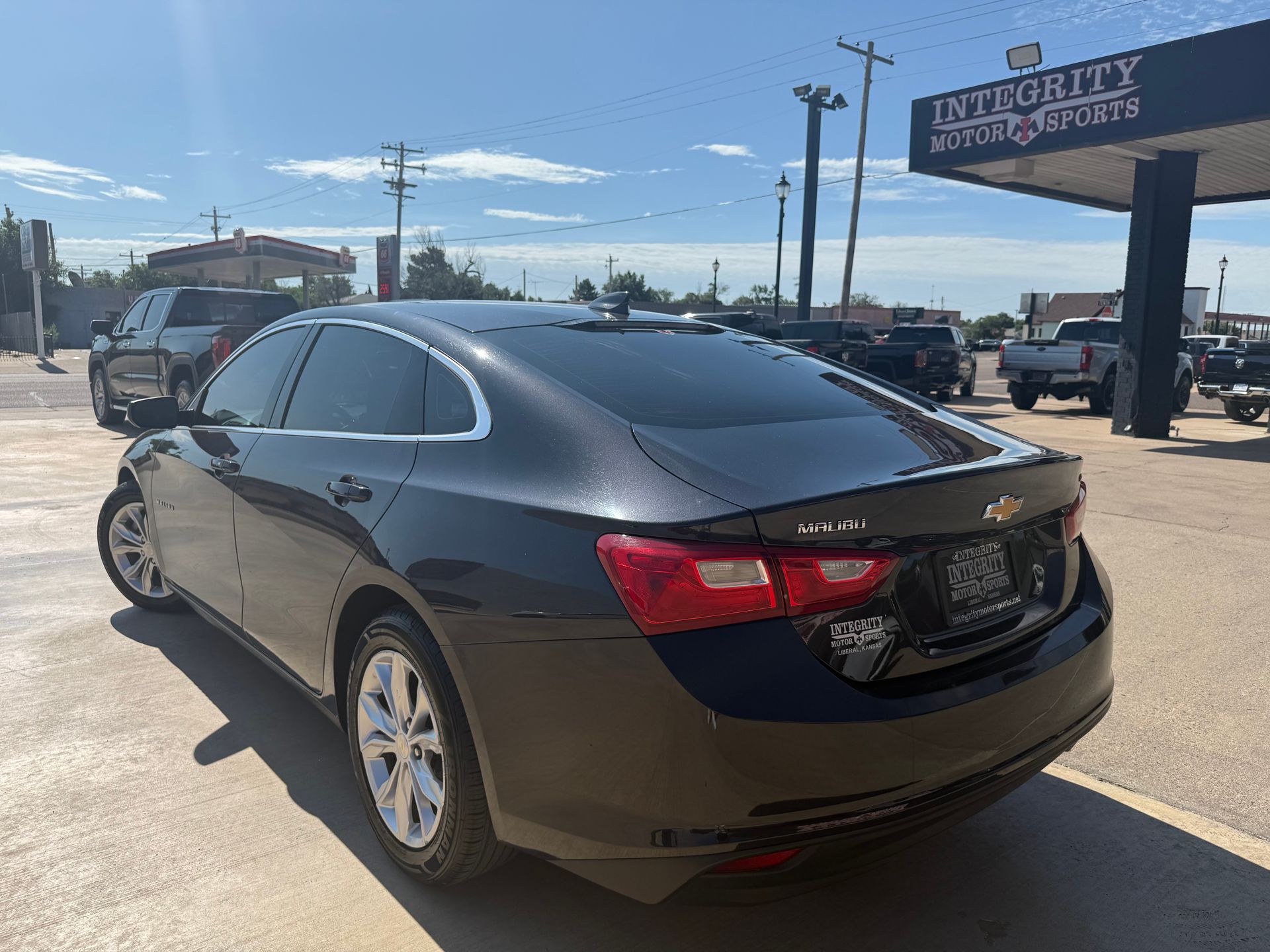 Dark gray Chevrolet Malibu parked outside a car dealership on a sunny day.