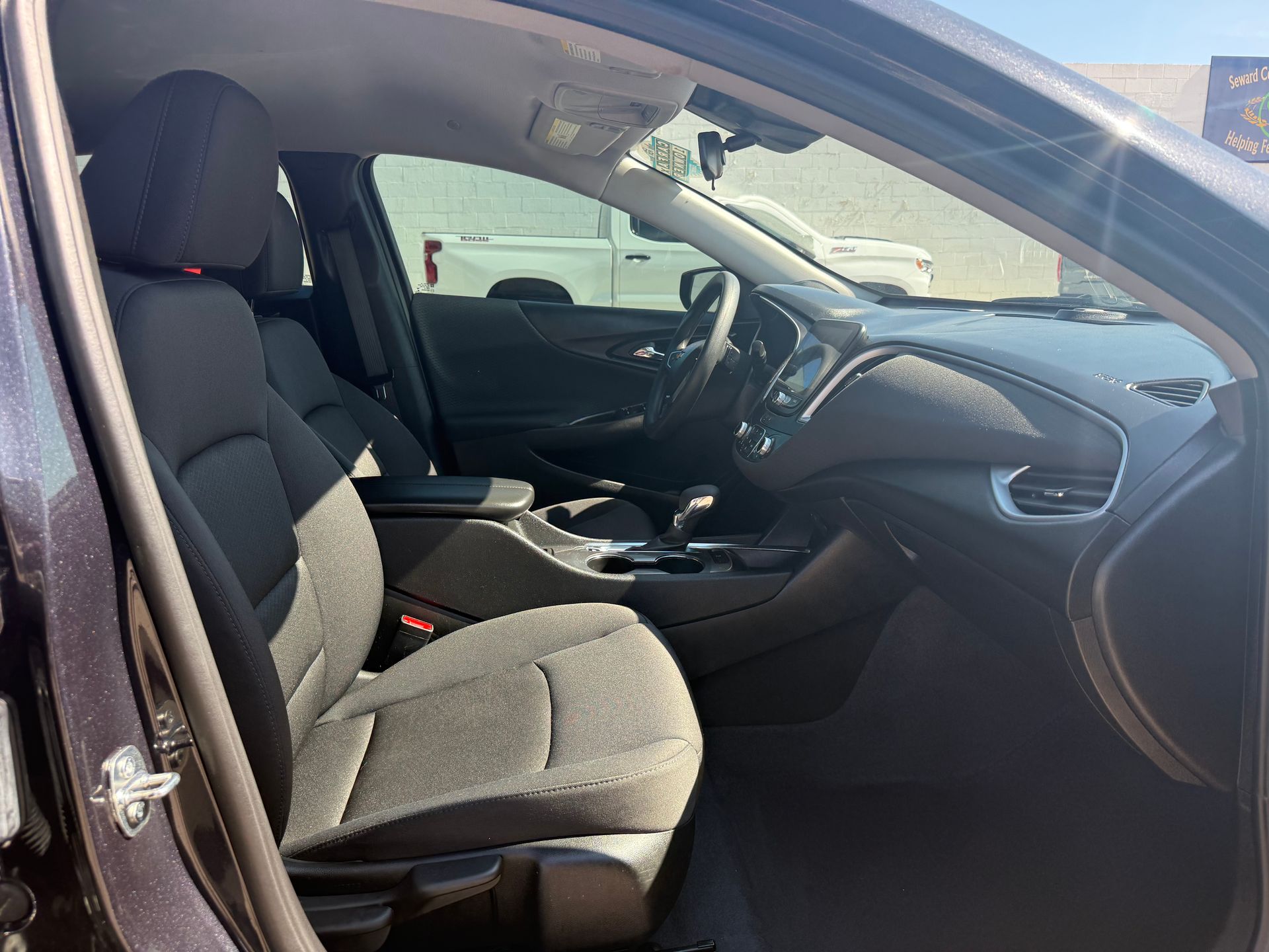 Interior of a dark car, showing driver's seat and dashboard. Bright sunlight streams through the windows.