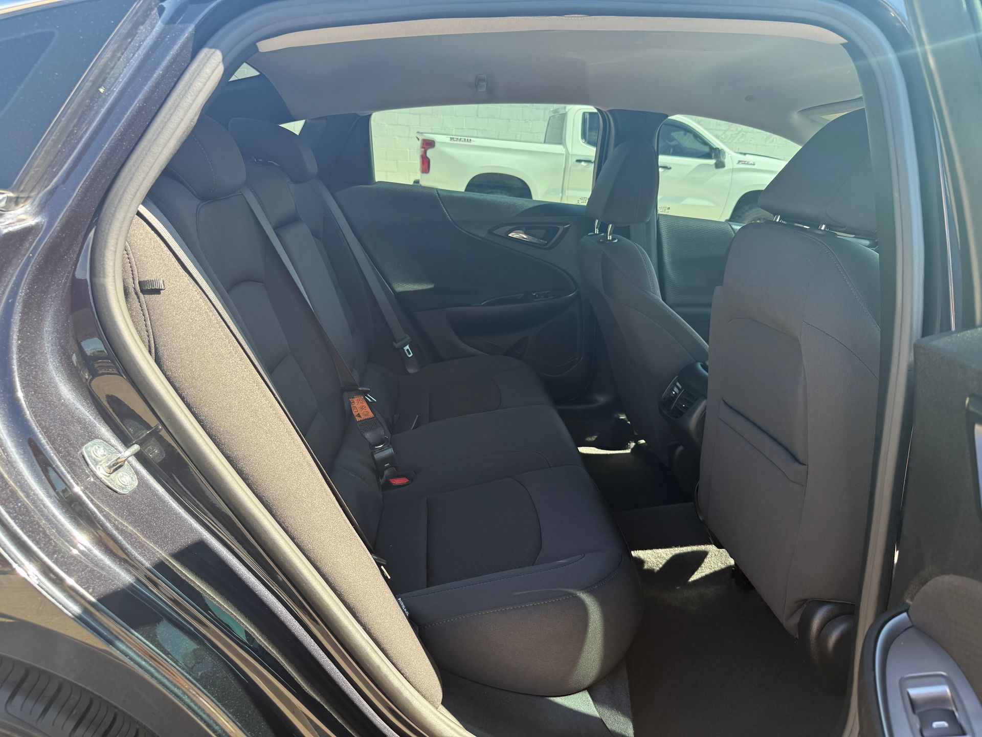 Interior back seat of a dark car, with black cloth seats and open door.