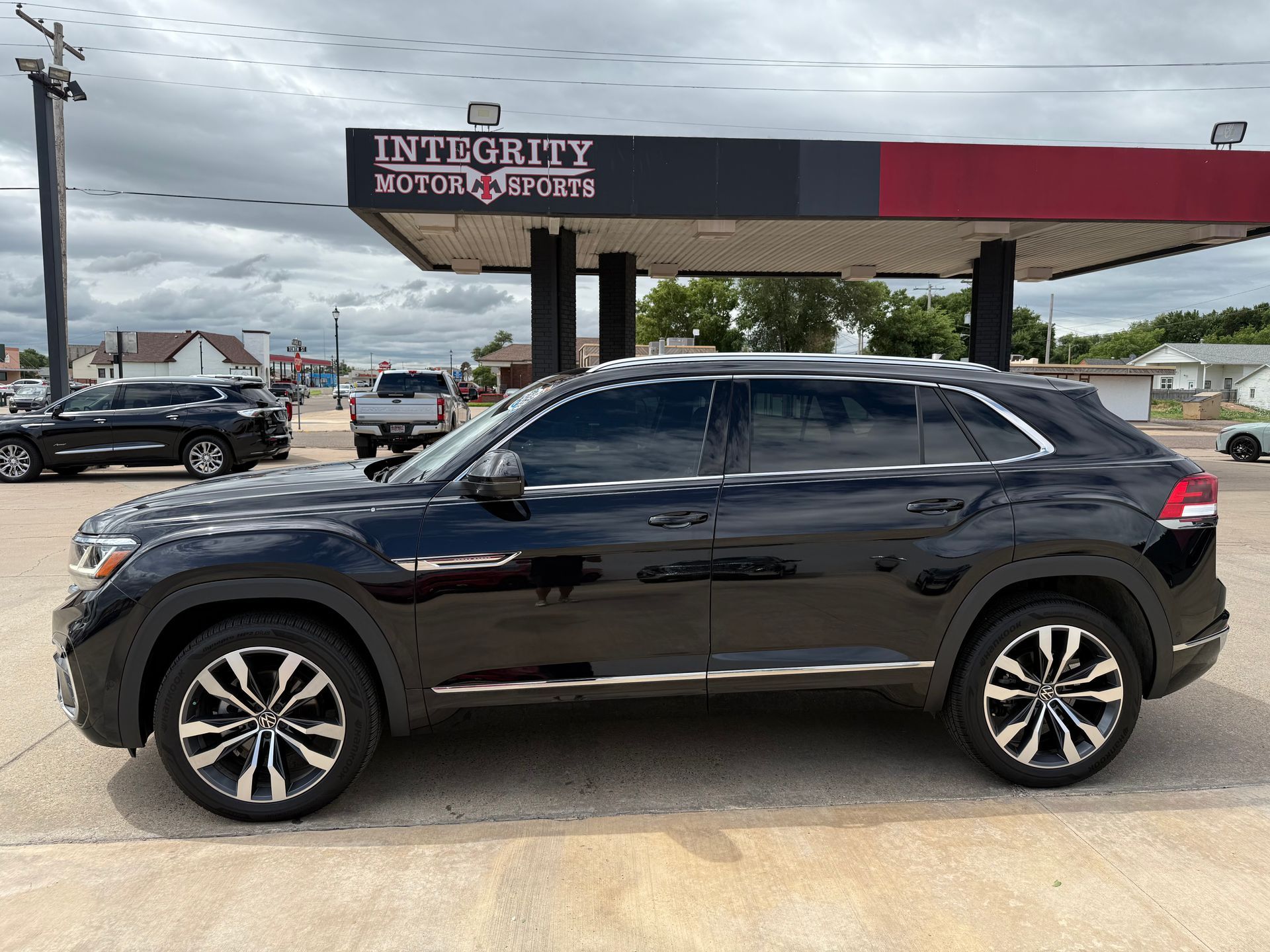 Black SUV parked in front of a car dealership with gas pumps under a cloudy sky.