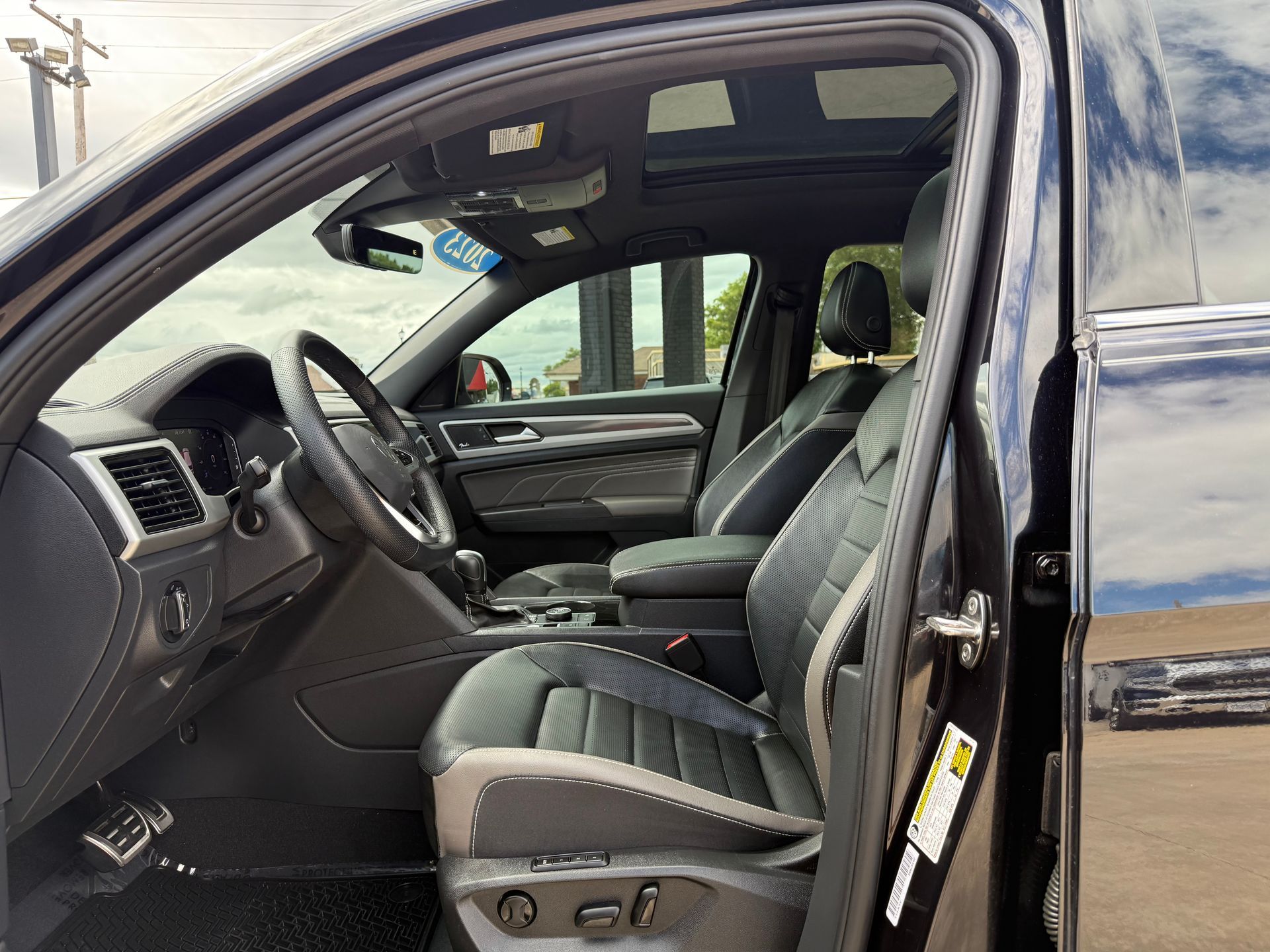 Black car interior with leather seats, steering wheel, and open sunroof.