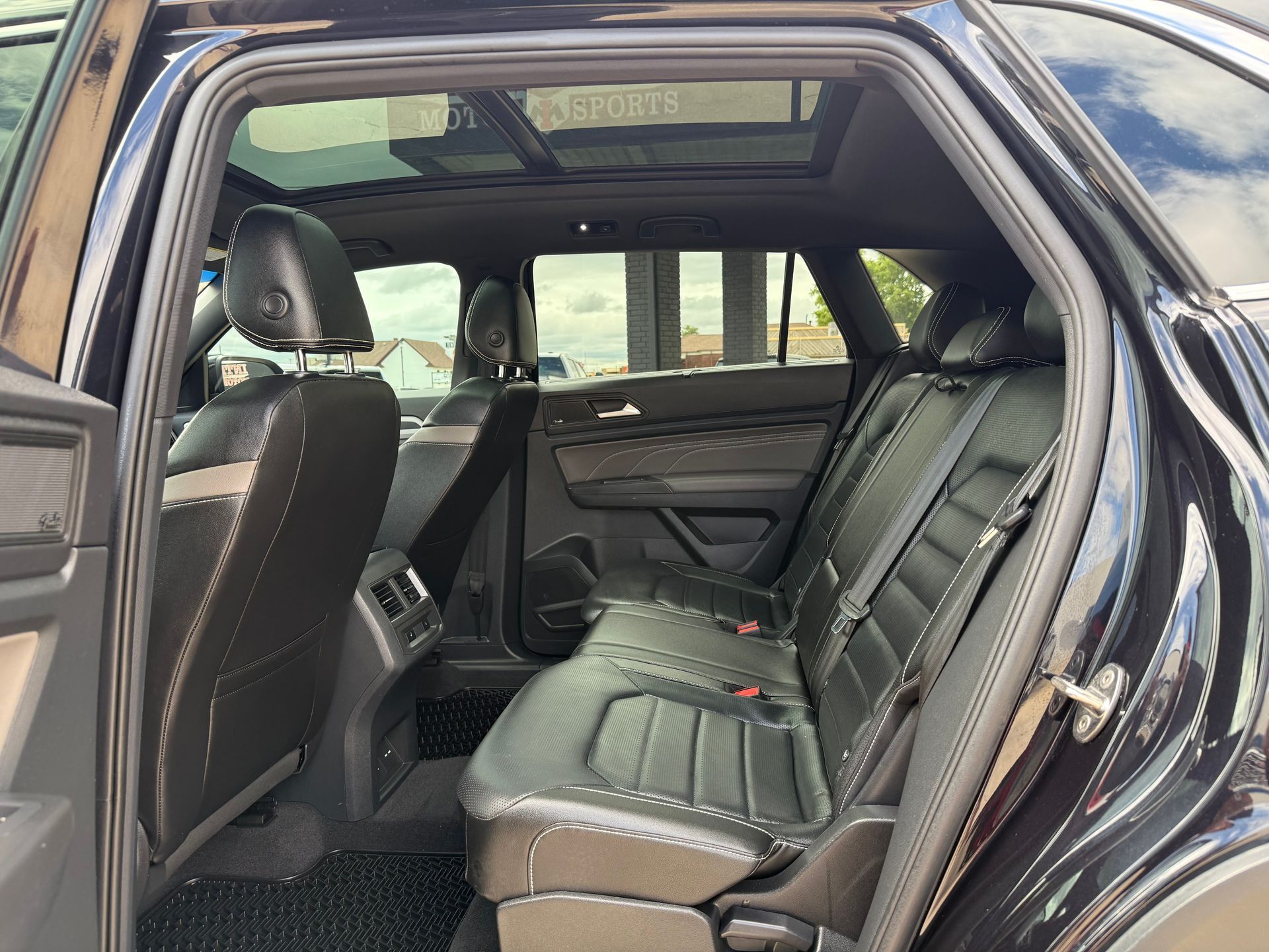 Interior of a black SUV, showing rear seats, sun roof, and open door.