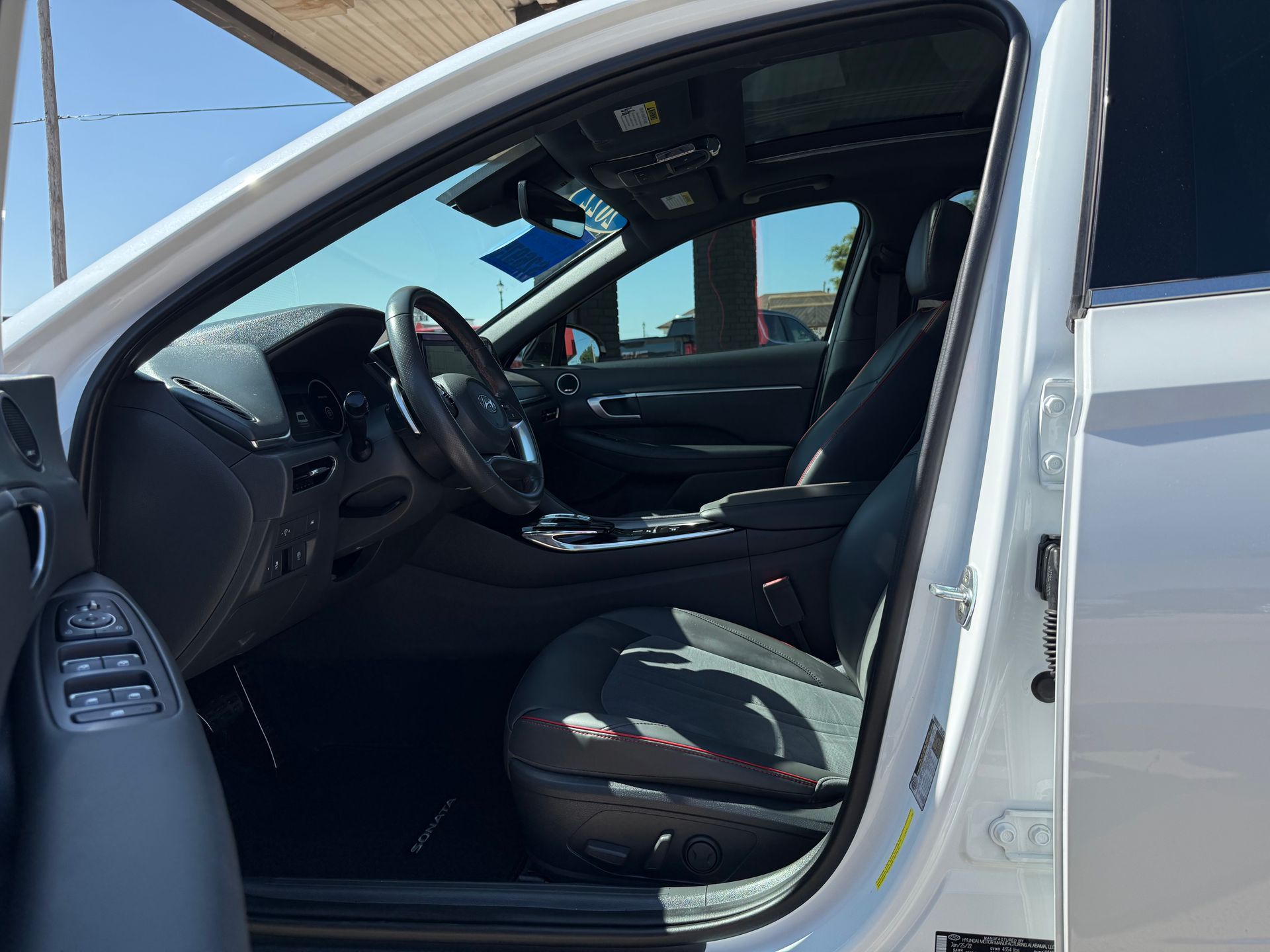 Interior of a white car with black seats and a driver's side door open on a sunny day.