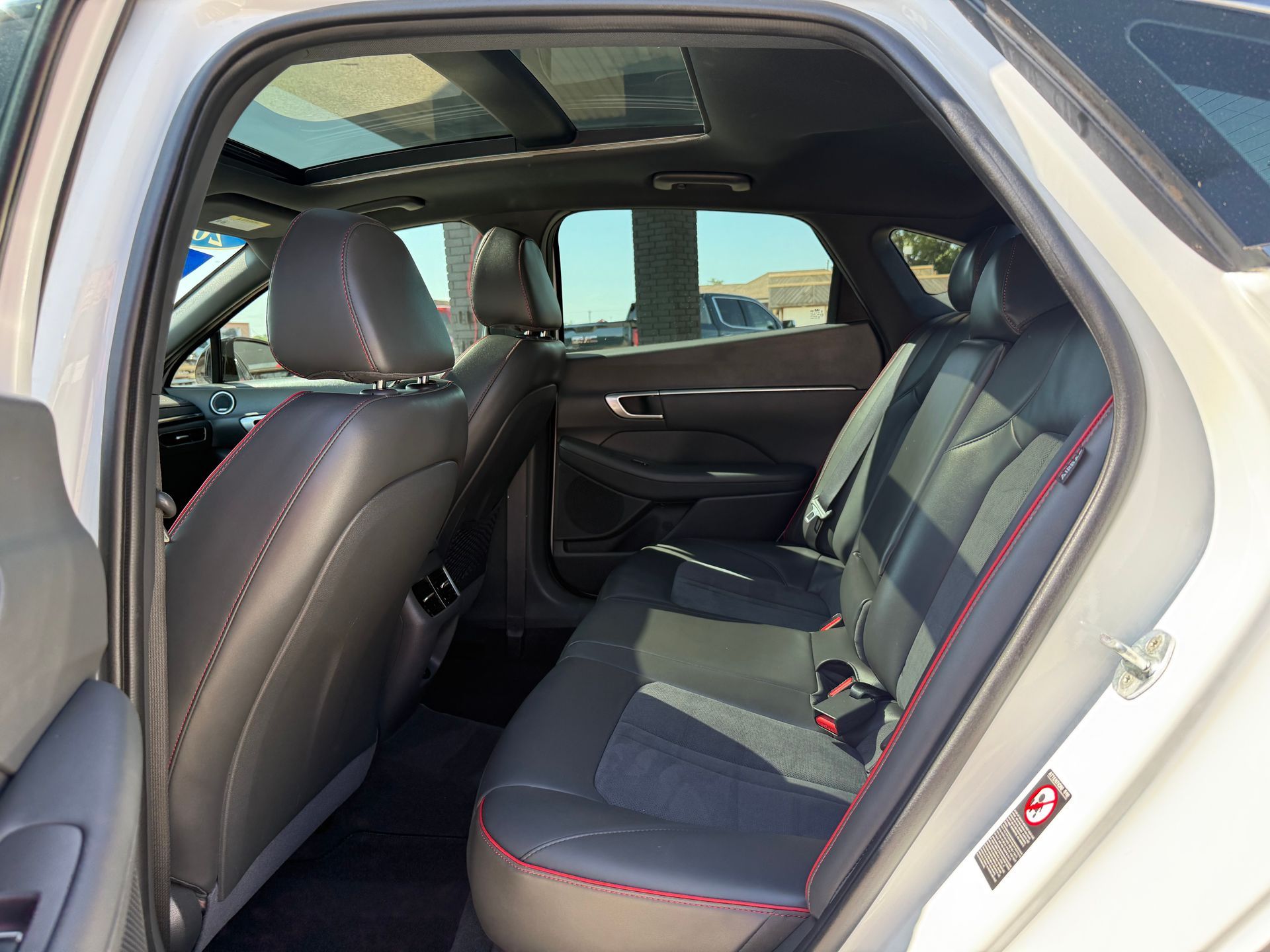 Back seat view of a white car interior with black leather seats, red stitching, and a sunroof.