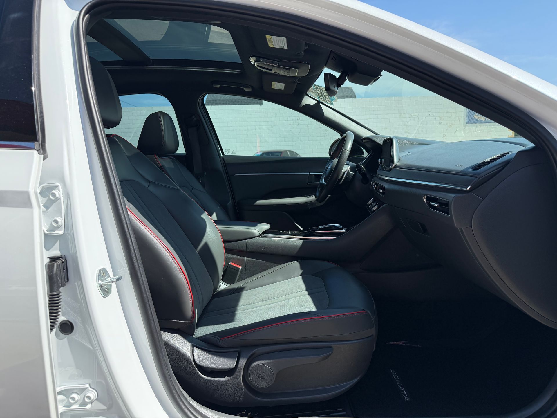 White car interior with black seats, panoramic sunroof, steering wheel, and dashboard.