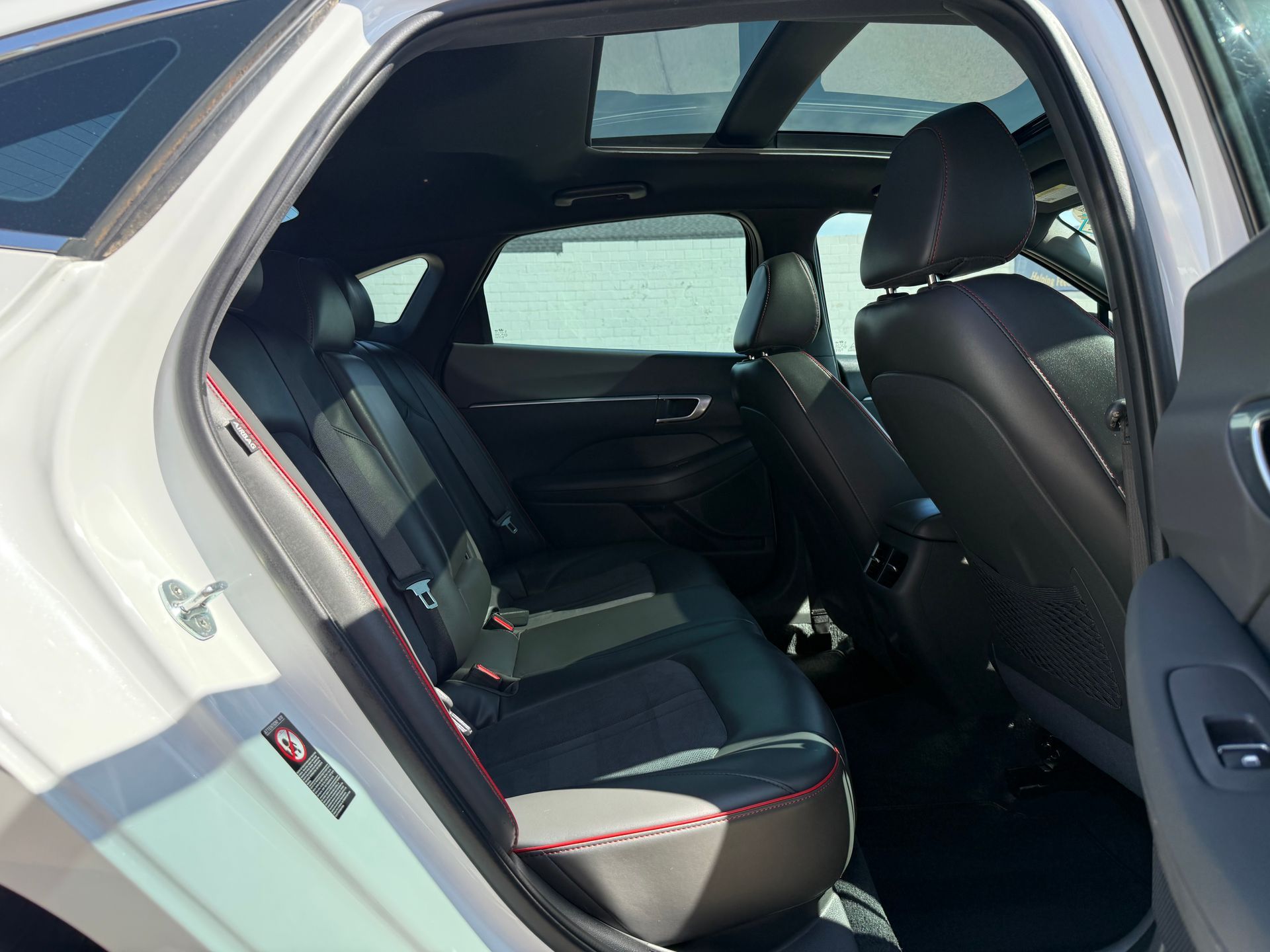 Interior view of a white car's backseat with black leather seats, a sunroof, and red stitching details.