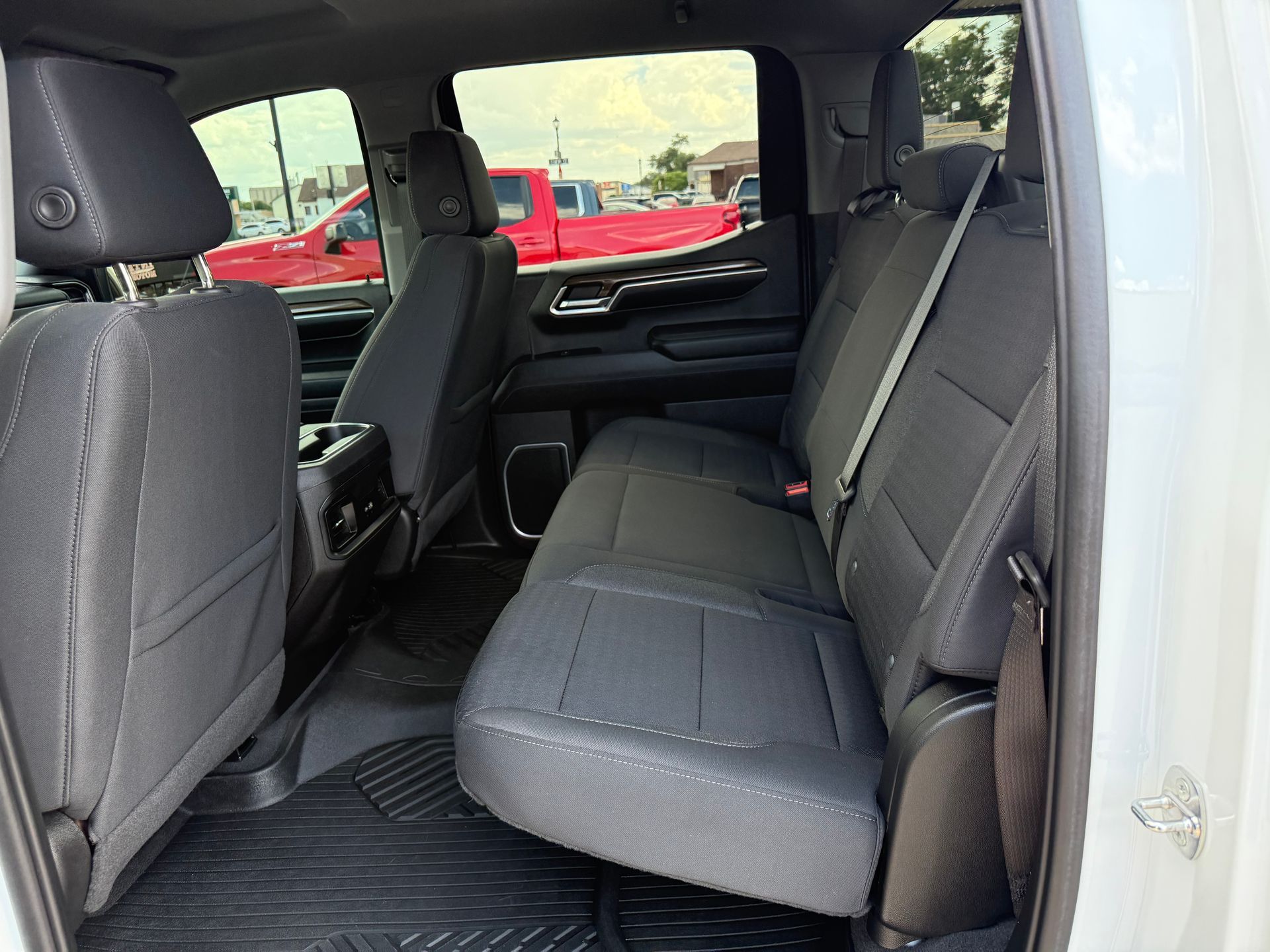 Interior view of a truck's back seat with black seats, window, and a red truck visible outside.