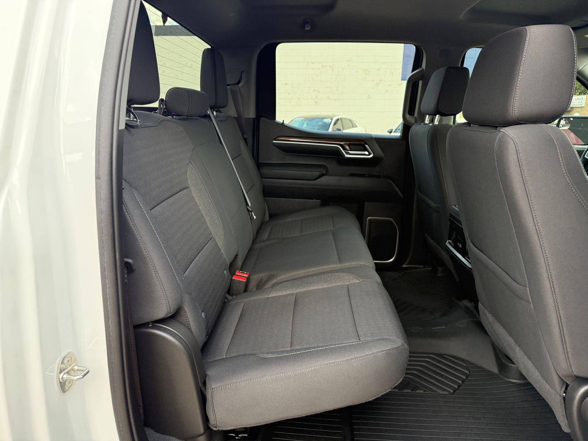 Interior of a truck's back seat, gray fabric seats, black floor mat, silver door handle, and tinted window.