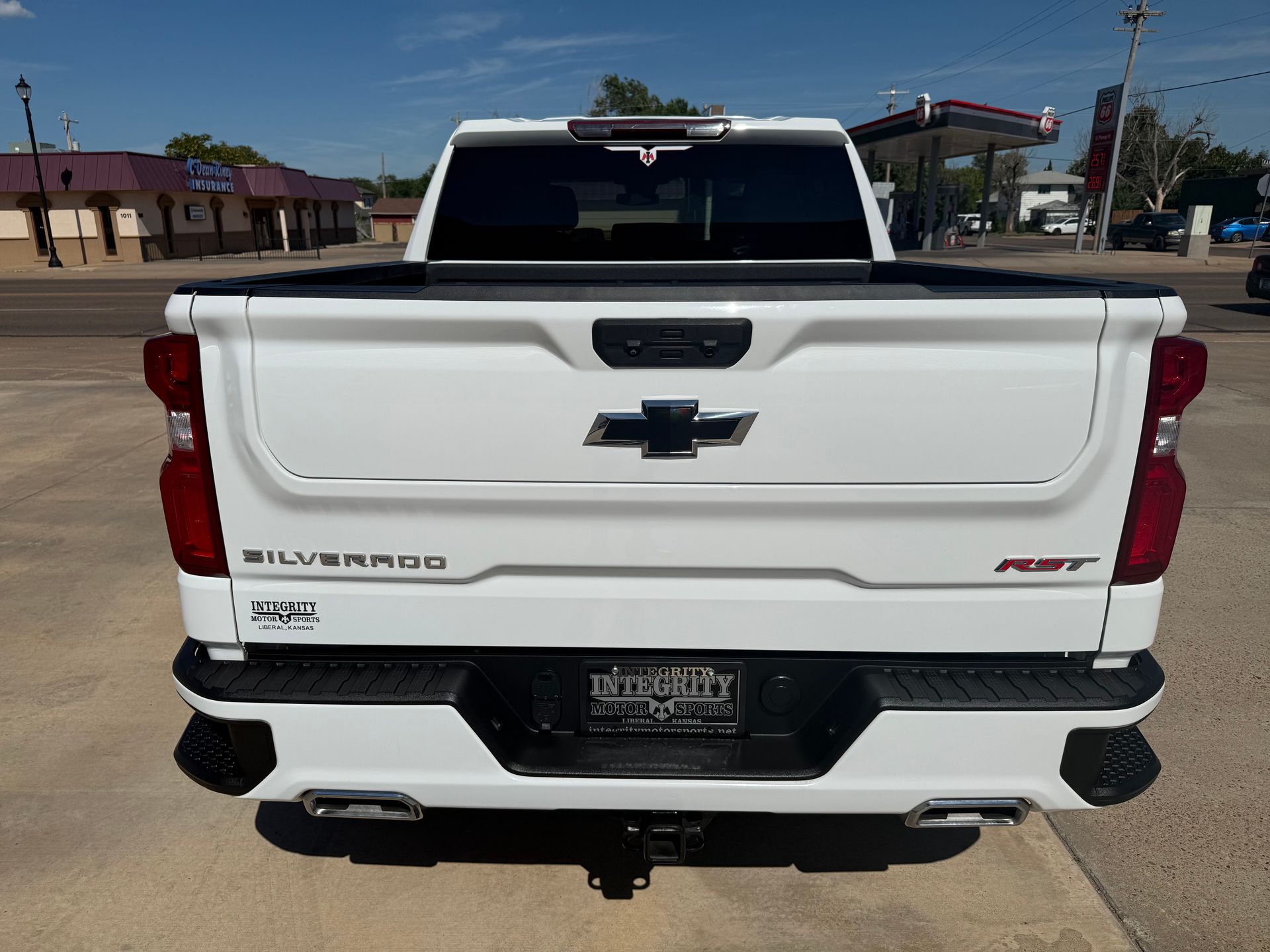 White Chevrolet Silverado pickup truck rear view with black accents, parked on a sunny street.