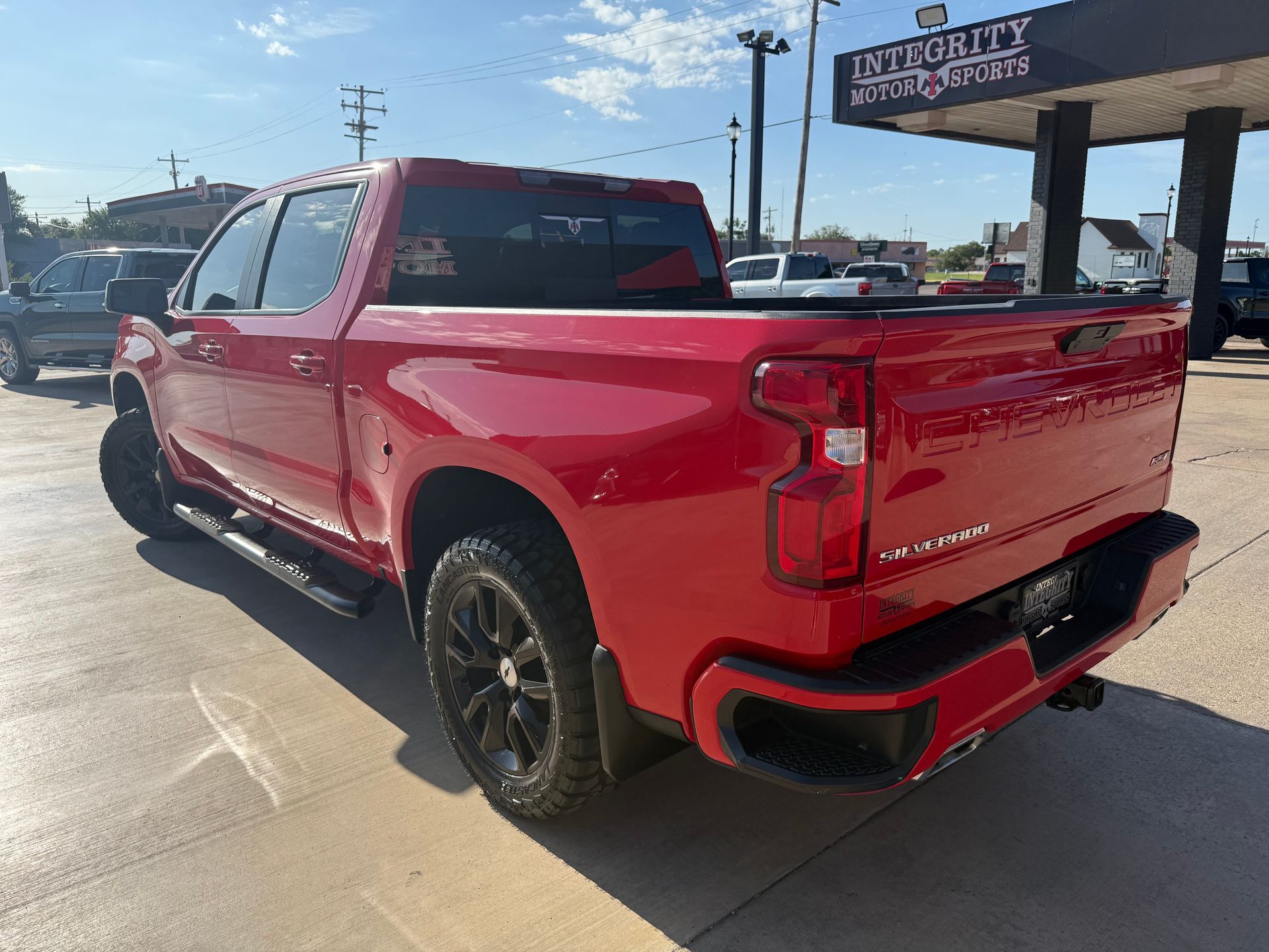 Red Chevy Silverado pickup truck parked outside a car dealership on a sunny day.