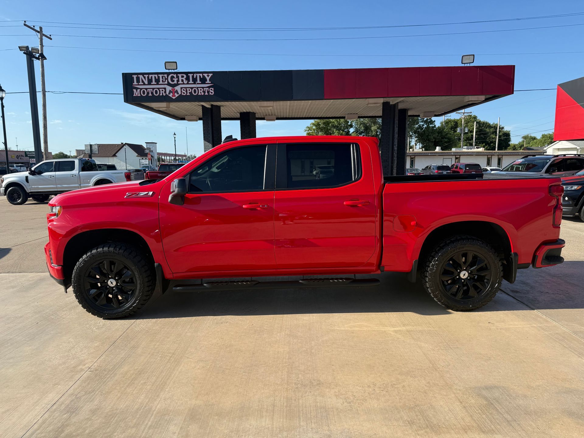Red Chevrolet pickup truck with black wheels parked in front of Integrity Auto Sports.