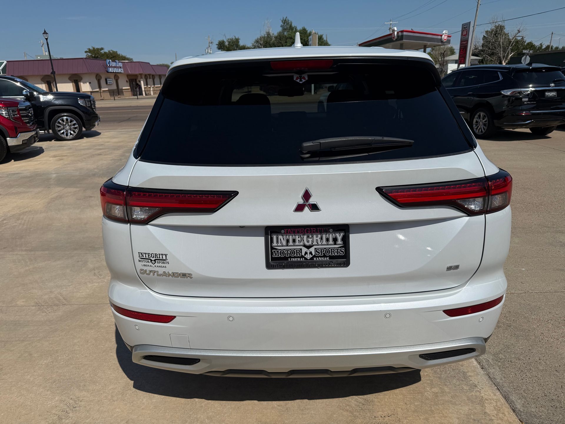 White Mitsubishi Outlander SUV, rear view, in a parking lot.