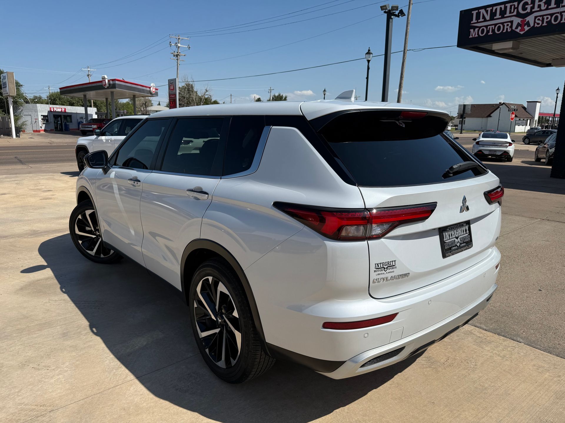 White Mitsubishi SUV parked outside a car dealership on a sunny day.