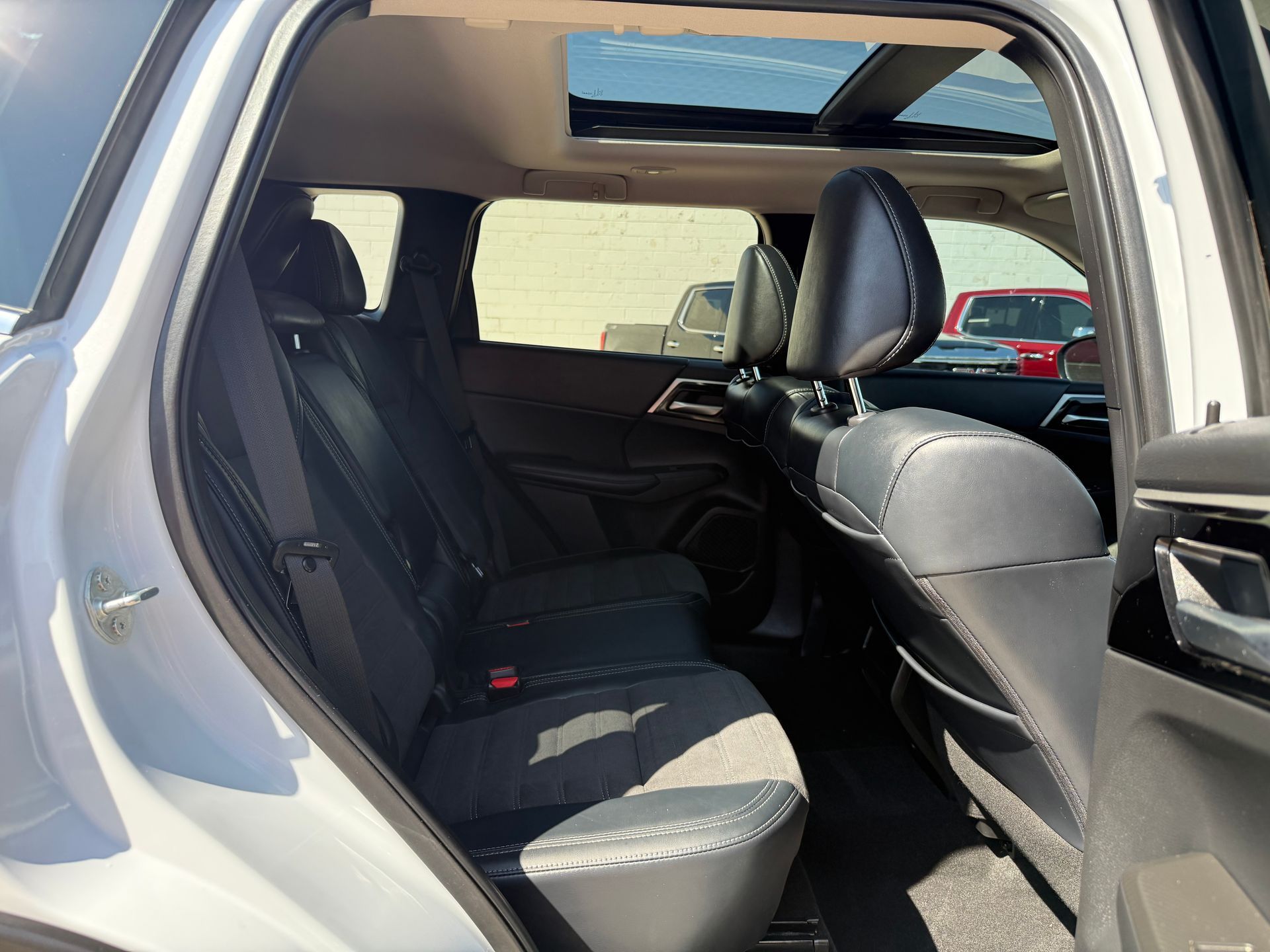 Rear passenger seats of a white SUV with a sunroof. Black leather and gray fabric seats.