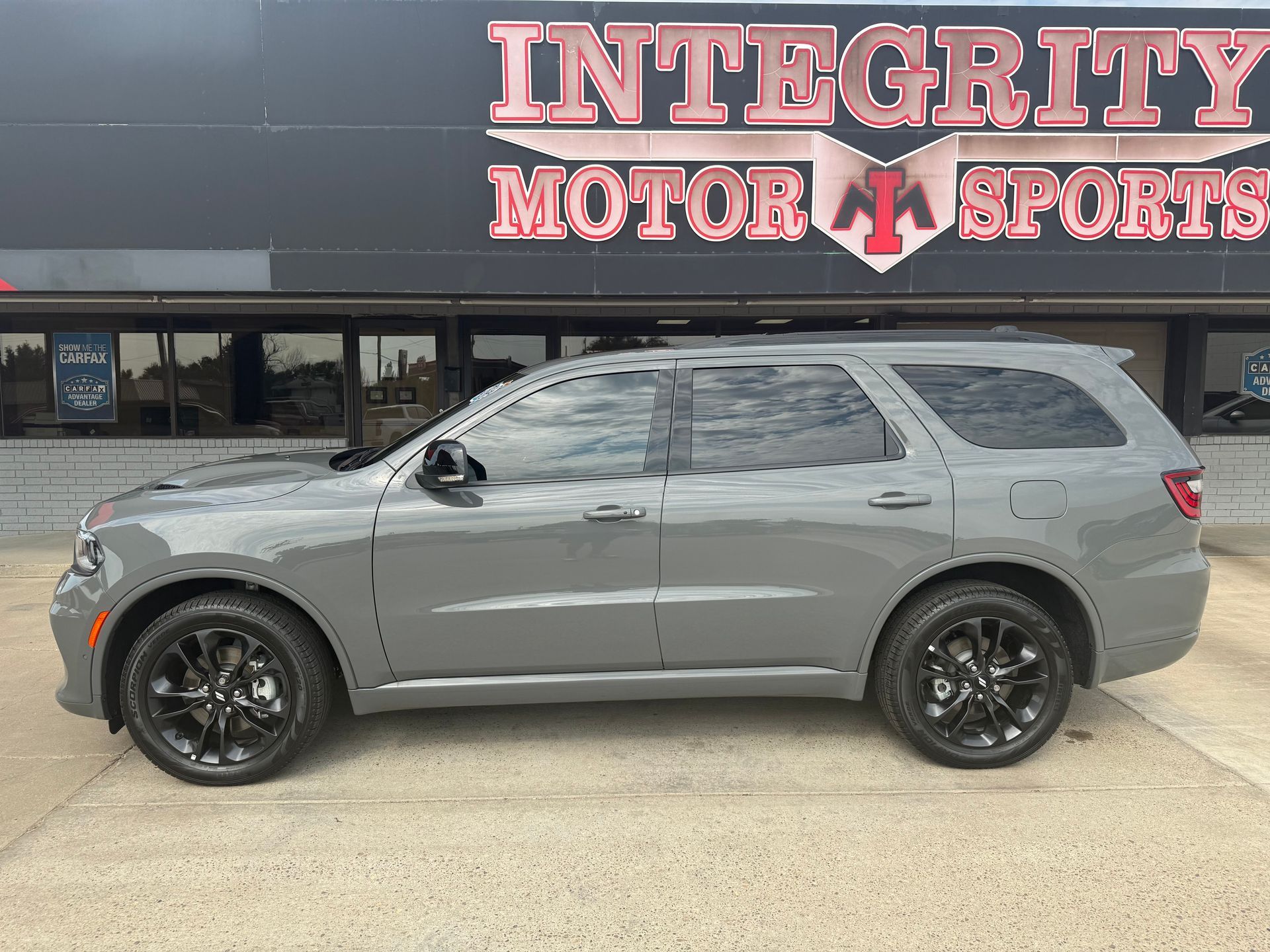 Gray Dodge Durango SUV parked in front of Integrity Motor Sports dealership. Black wheels, tinted windows.