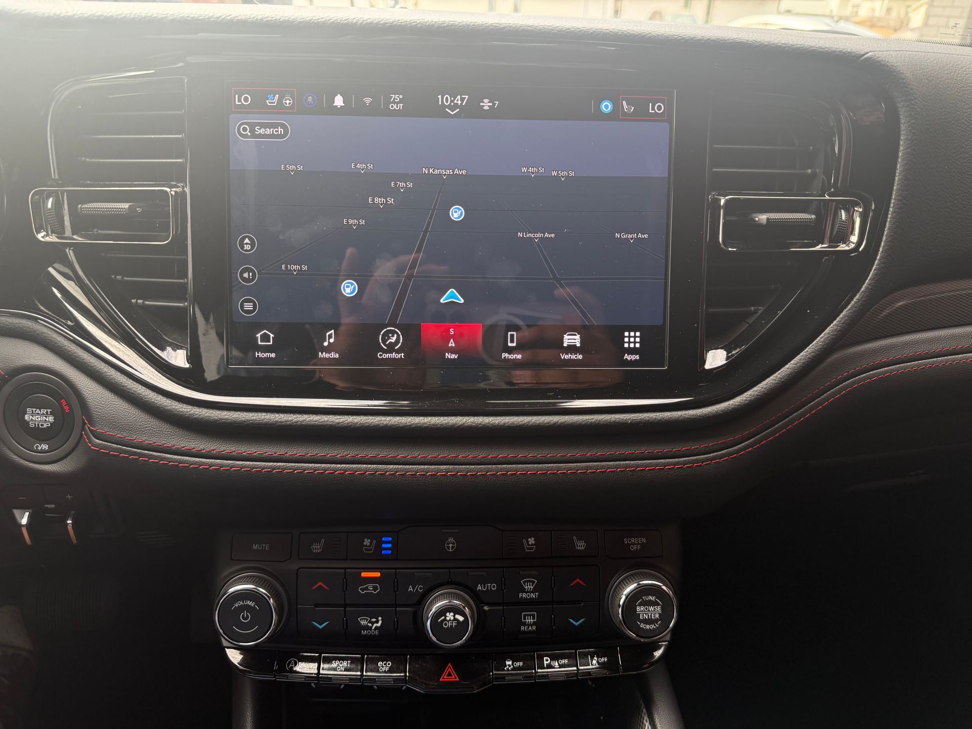 Dashboard of a vehicle with a navigation screen displaying a map. Black interior, with red accent stitching.