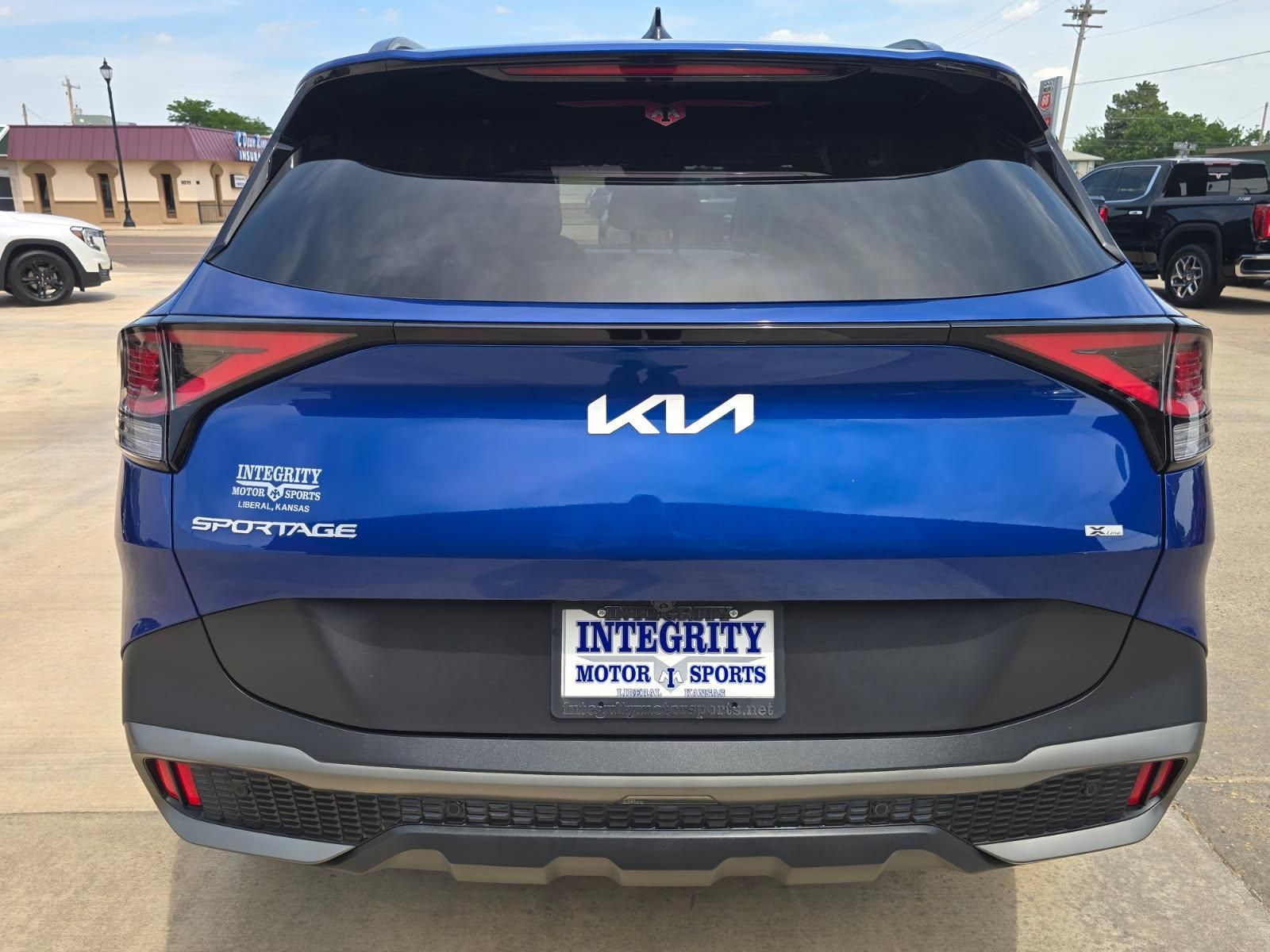Rear view of a blue Kia SUV parked outside an Integrity Auto Sales lot