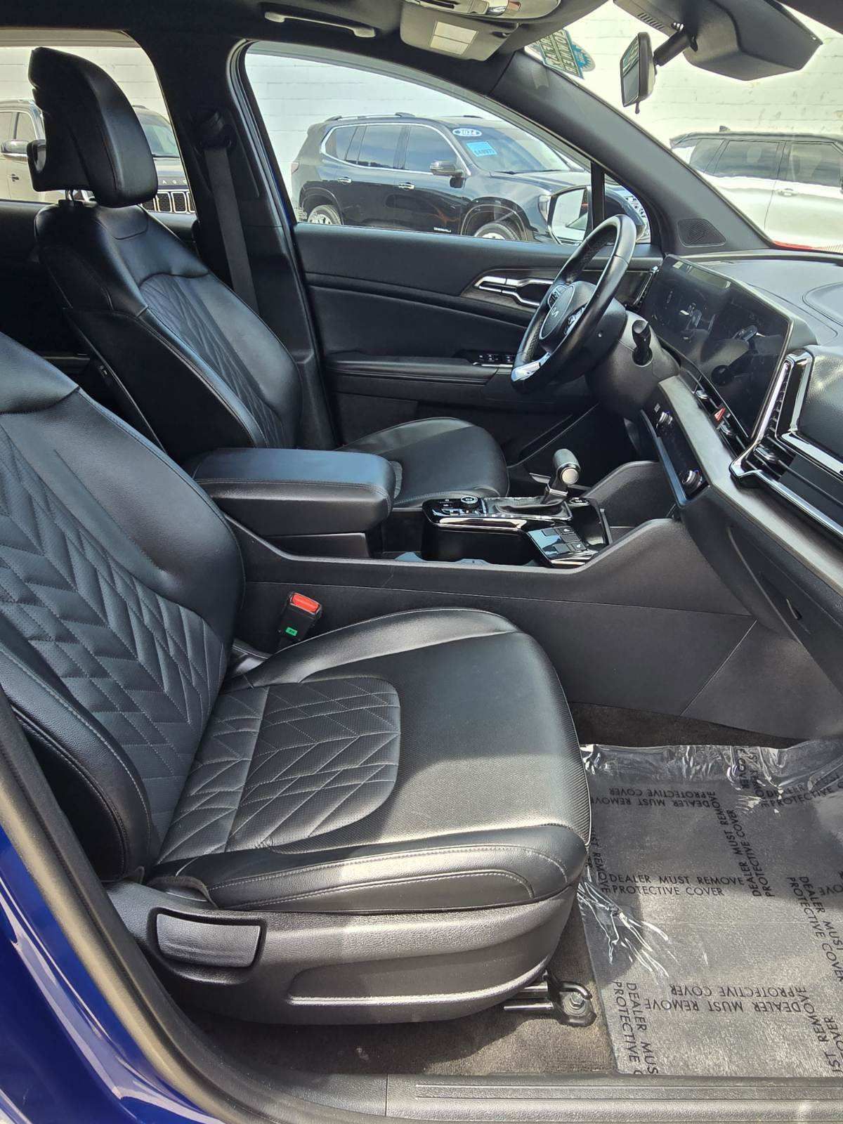 Black car interior with diamond-stitched seats and center console, viewed from the open passenger door
