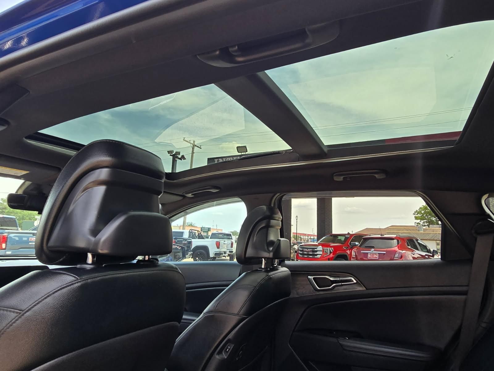 Car interior with panoramic glass roof and black leather seats, parked in a lot.