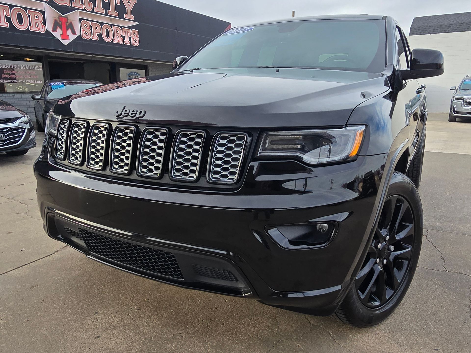 Black Jeep Grand Cherokee parked in front of a car dealership.