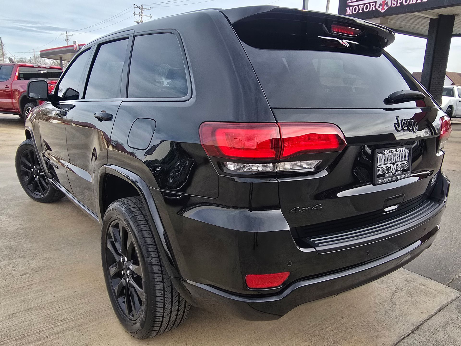Black Jeep Grand Cherokee SUV with black rims parked outside a car dealership.