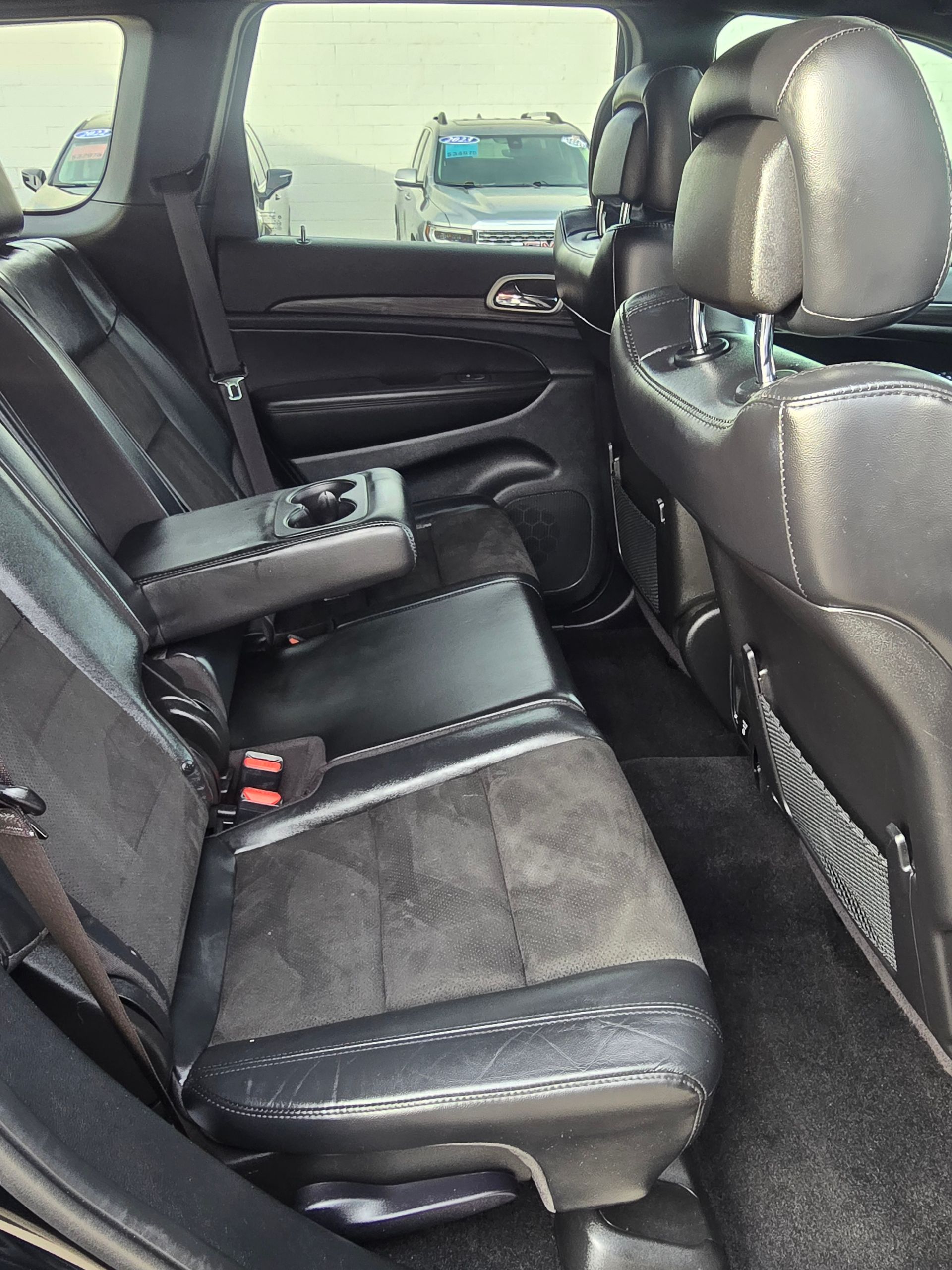 Black leather and suede car backseats with armrest, cup holders, and headrests; daylight setting.