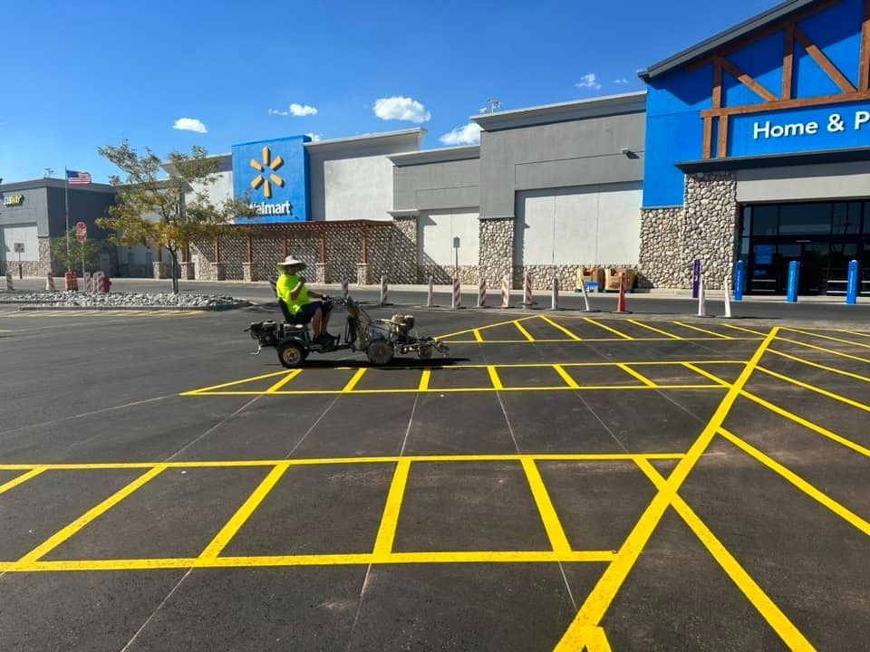 Worker on a machine painting yellow parking lines at a Walmart store. Bright sunny day, blue sky.