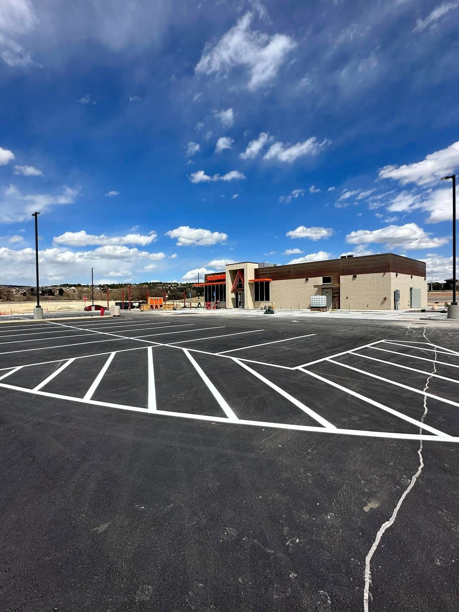 Newly paved parking lot with marked spaces in front of a modern building under a blue sky.