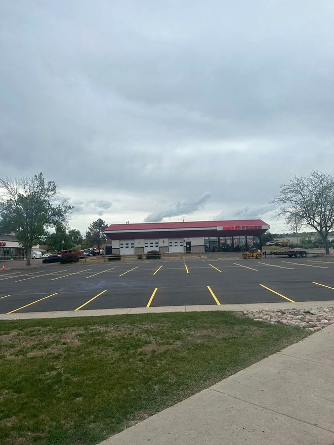 Large commercial building with a red and white facade, surrounded by an empty parking lot on a cloudy day.
